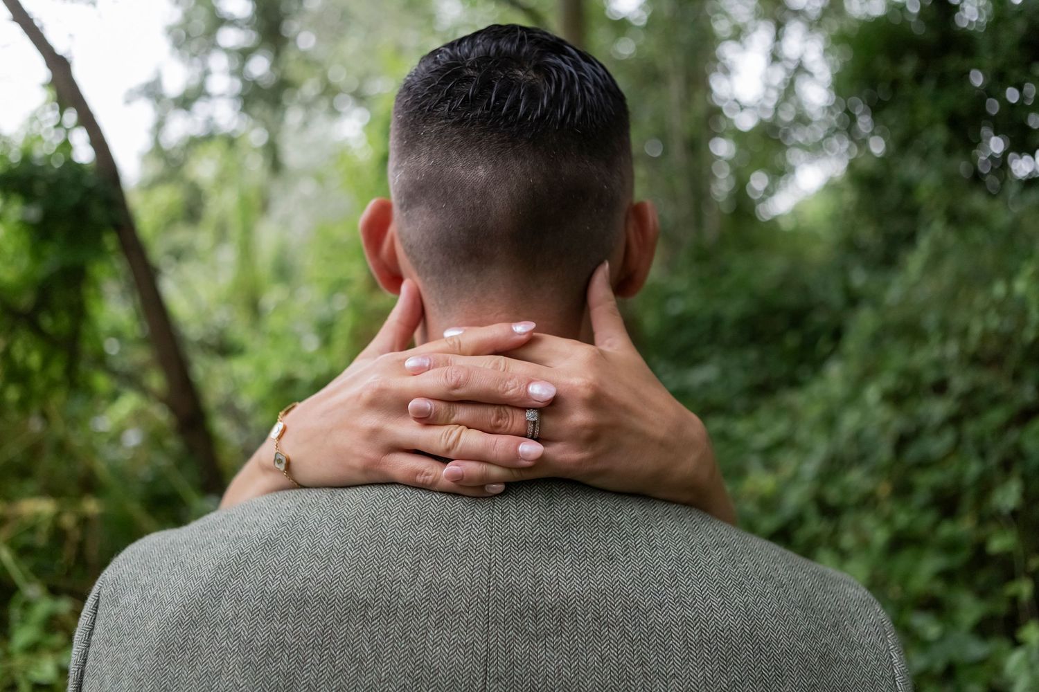 Close-up view of a groom in a grey suit from behind during an outdoor photoshoot.
