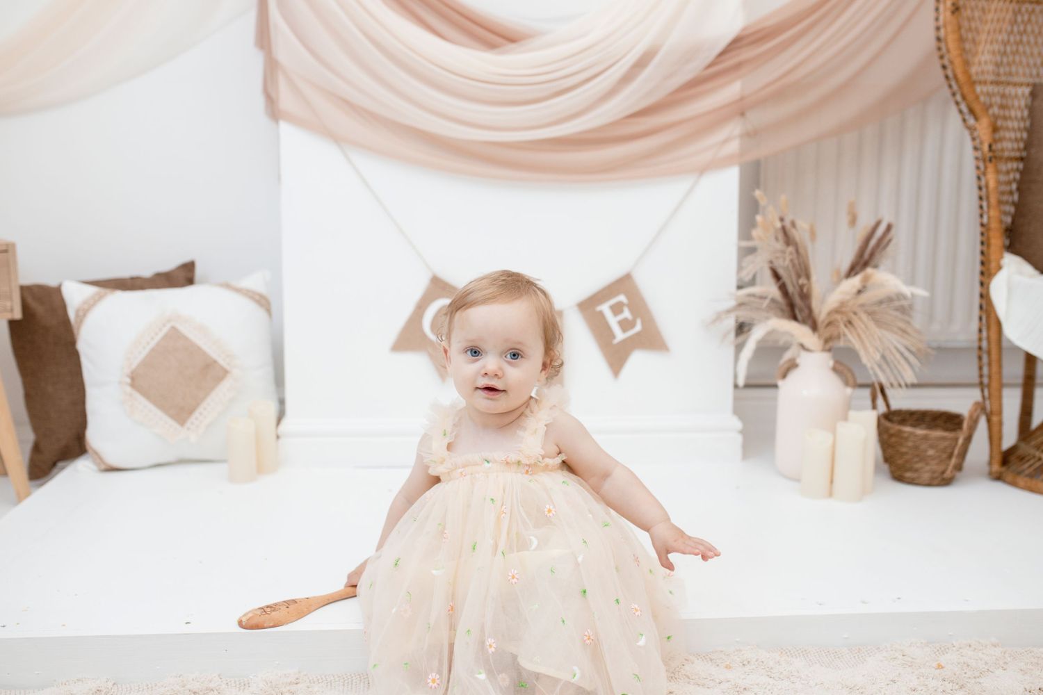 Neutral-toned cake smash photo setup with rustic banner decorations and wooden accents.