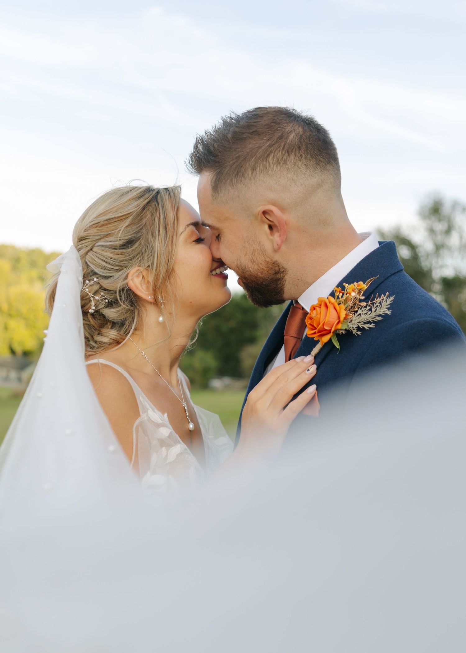 A romantic wedding portrait with an orange boutonniere against a soft background.