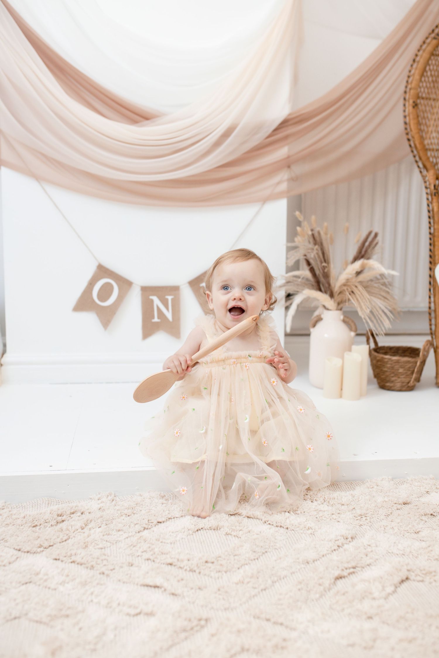 Baby in cream tulle dress celebrating first birthday with rustic decorations and banner.
