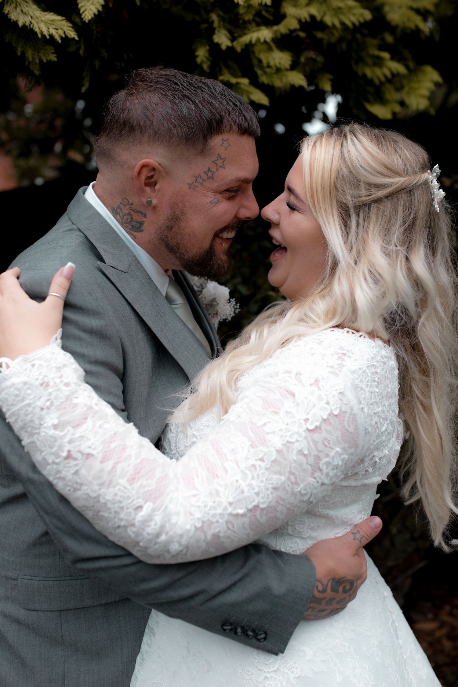 Romantic wedding couple embracing outdoors in gray suit and white lace dress.