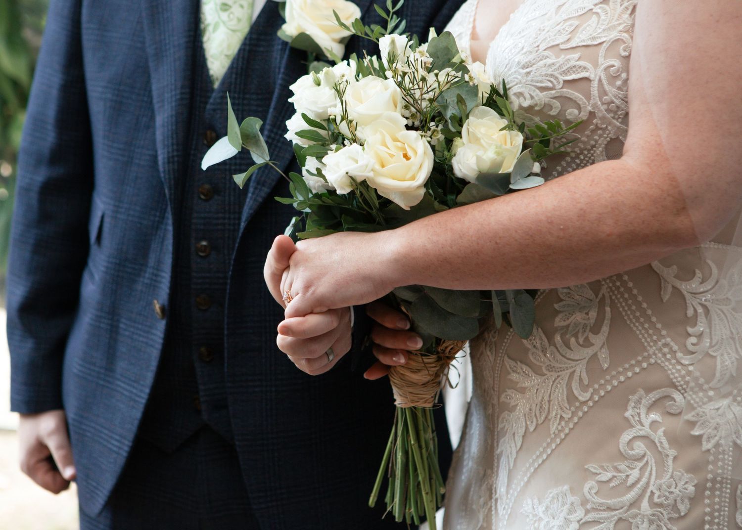 Elegant white rose wedding bouquet held against a lace bridal gown.