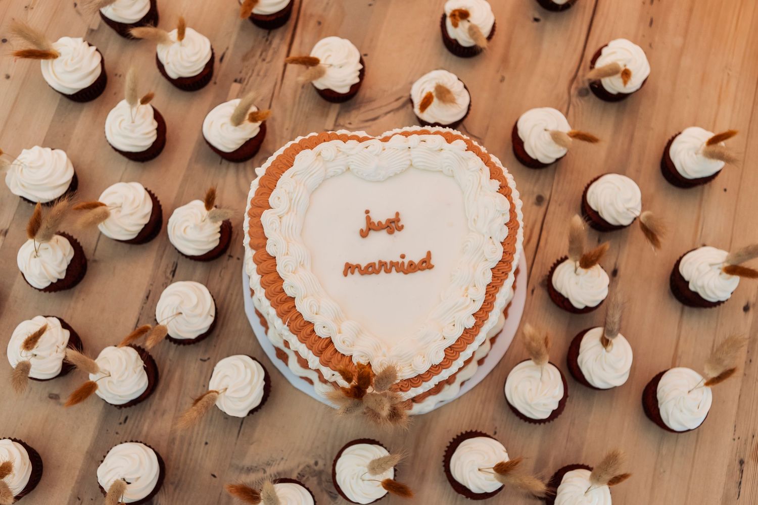 Overhead view of white cupcakes arranged on a wooden surface at a wedding reception.