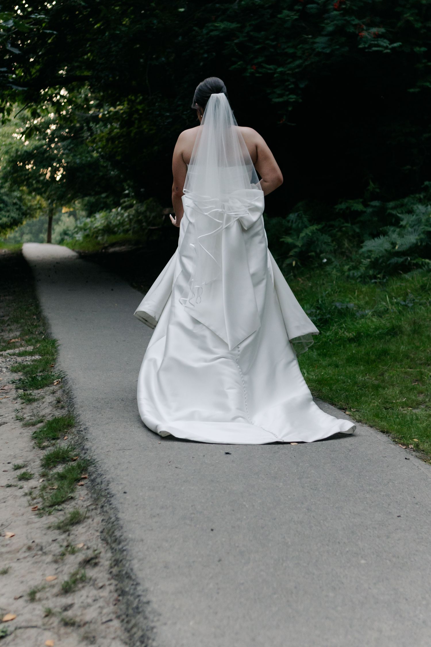 White wedding dress flowing elegantly on a garden path during an outdoor photoshoot.