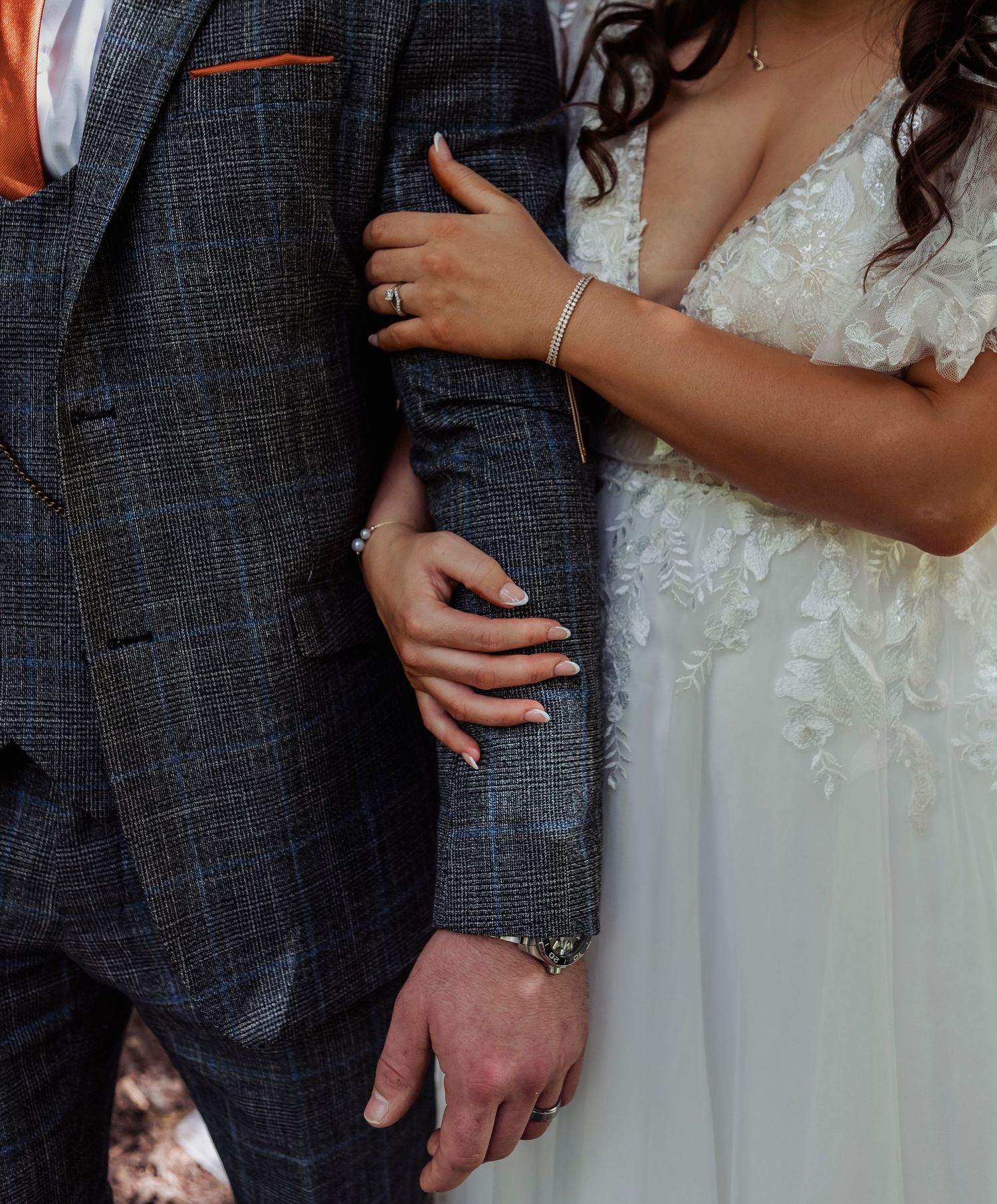 Close-up details of a bride and groom's wedding attire showing a grey tweed suit and white lace dress.