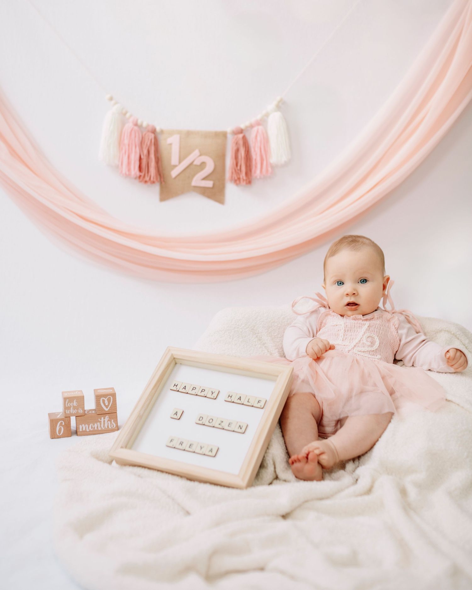 Baby in pink dress at 6 month milestone photo shoot with pink decorations and letter board.