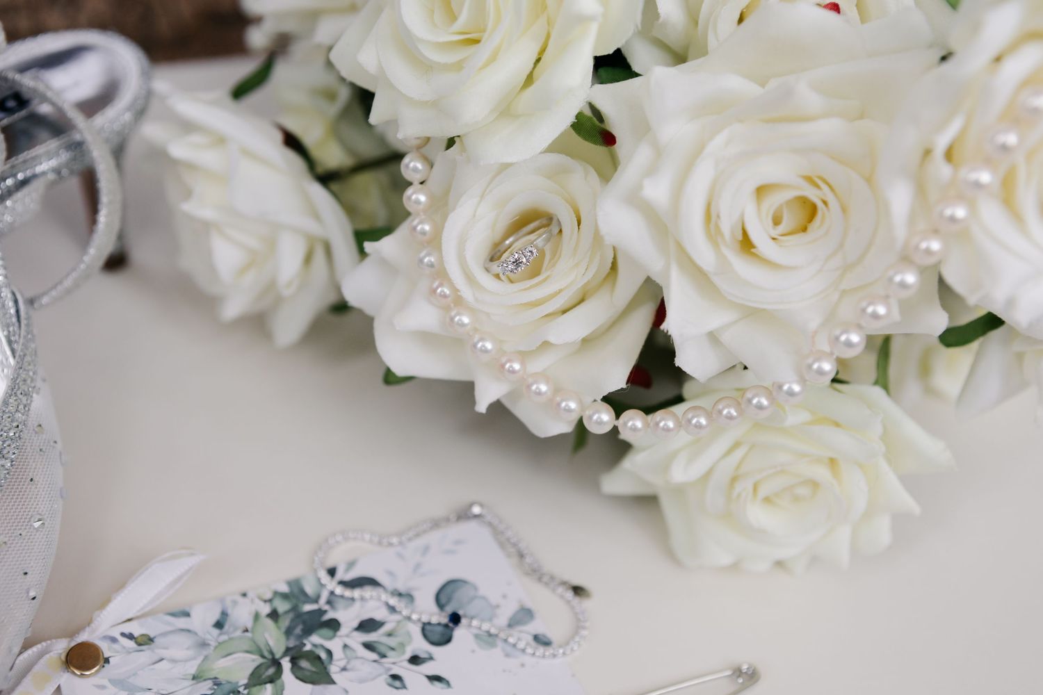Elegant white roses arranged with pearl details and wedding stationery.