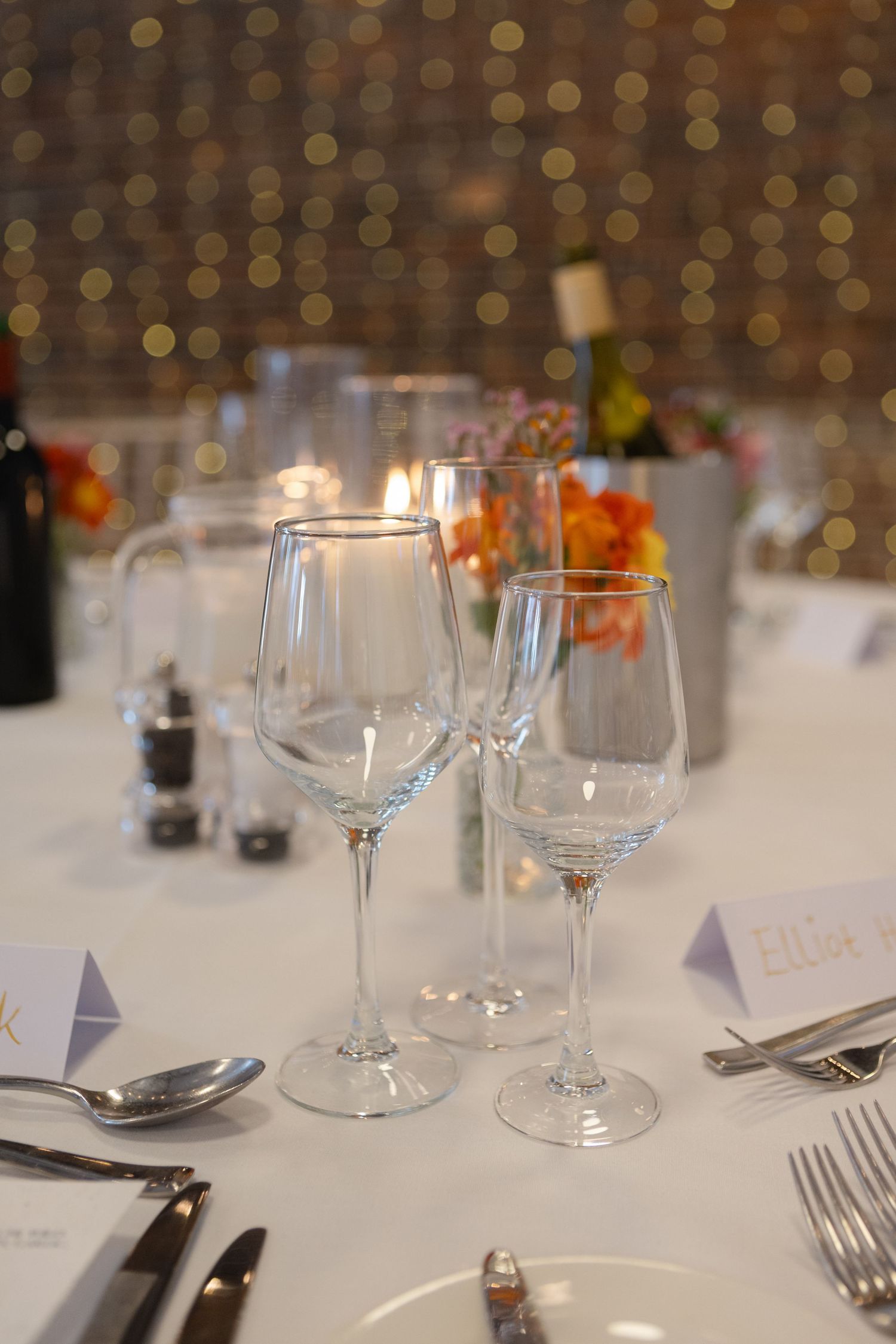 Close-up of formal table settings with wine glasses against bokeh lights.