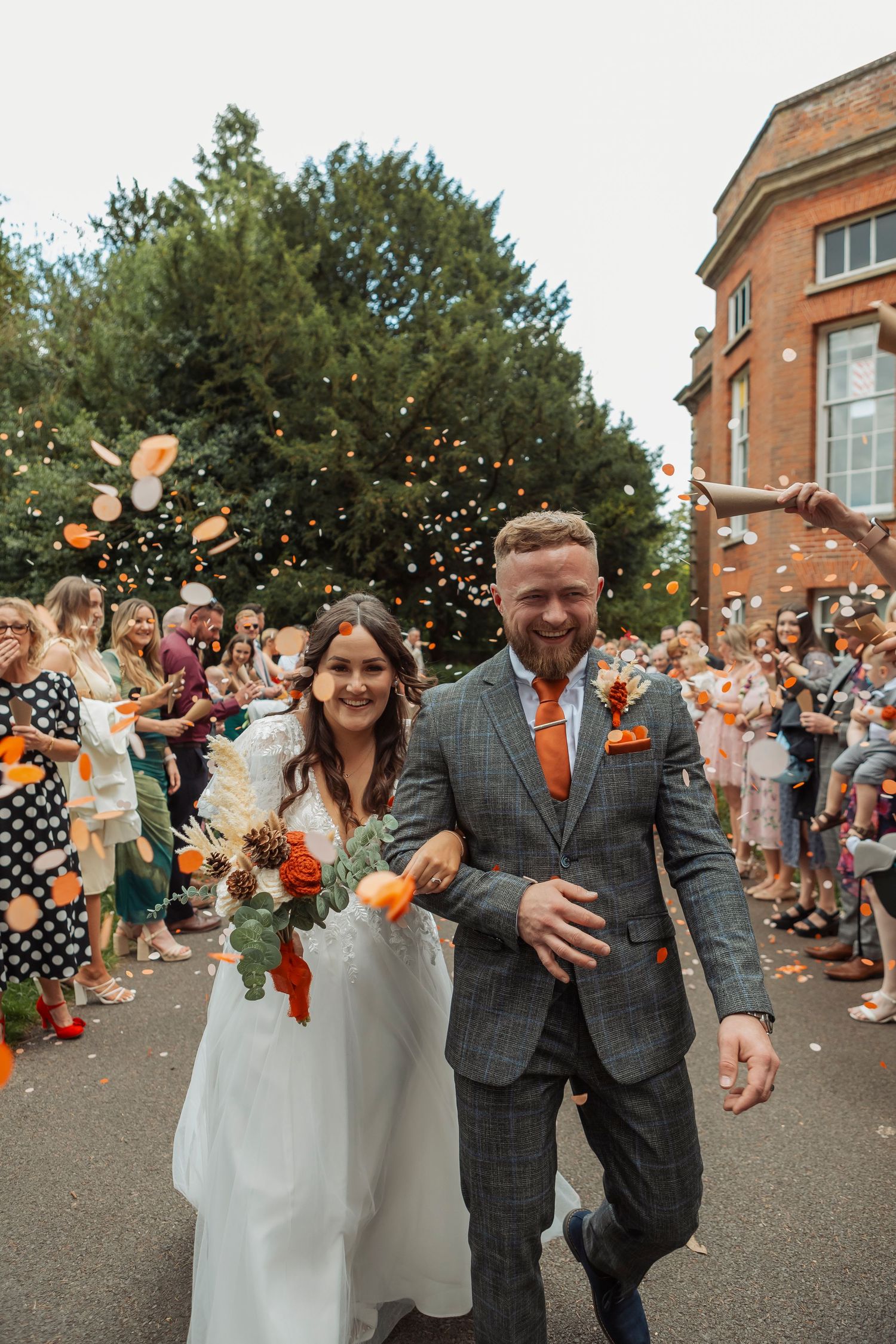 Joyful wedding recessional with guests throwing confetti outside brick building.