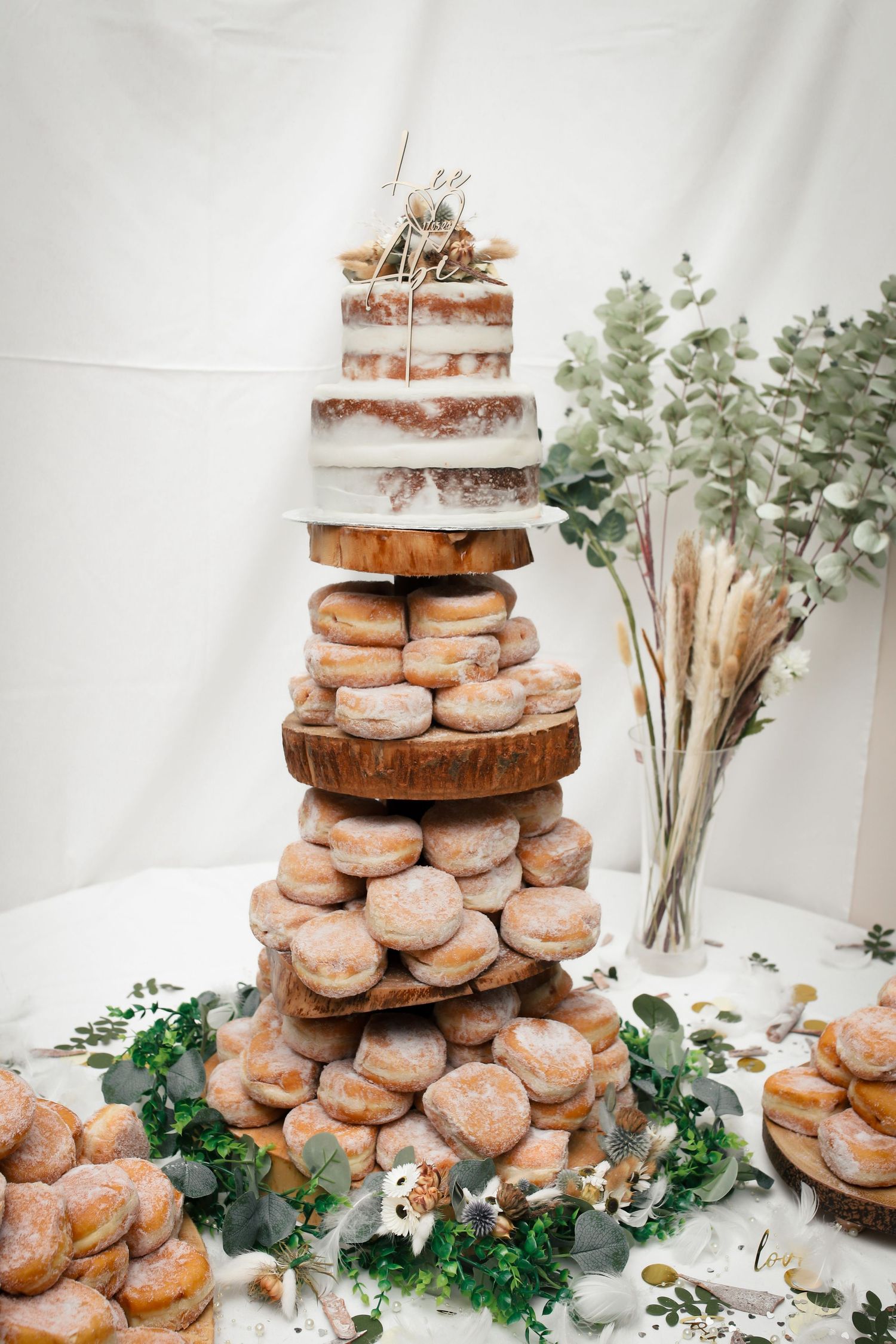 Tiered donut wedding cake display decorated with eucalyptus and wooden stands.