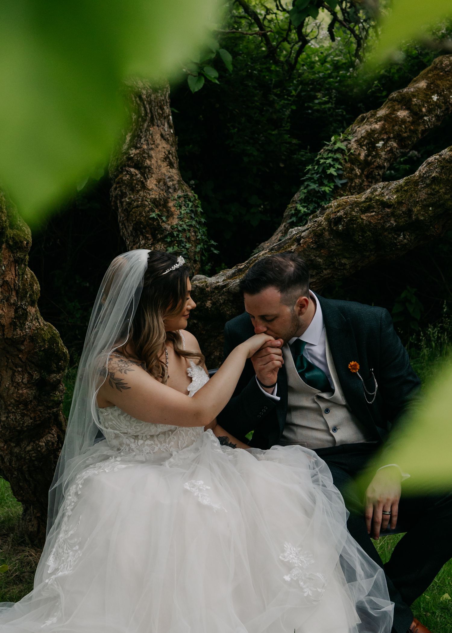 Romantic wedding portrait captured through foliage in a garden setting.