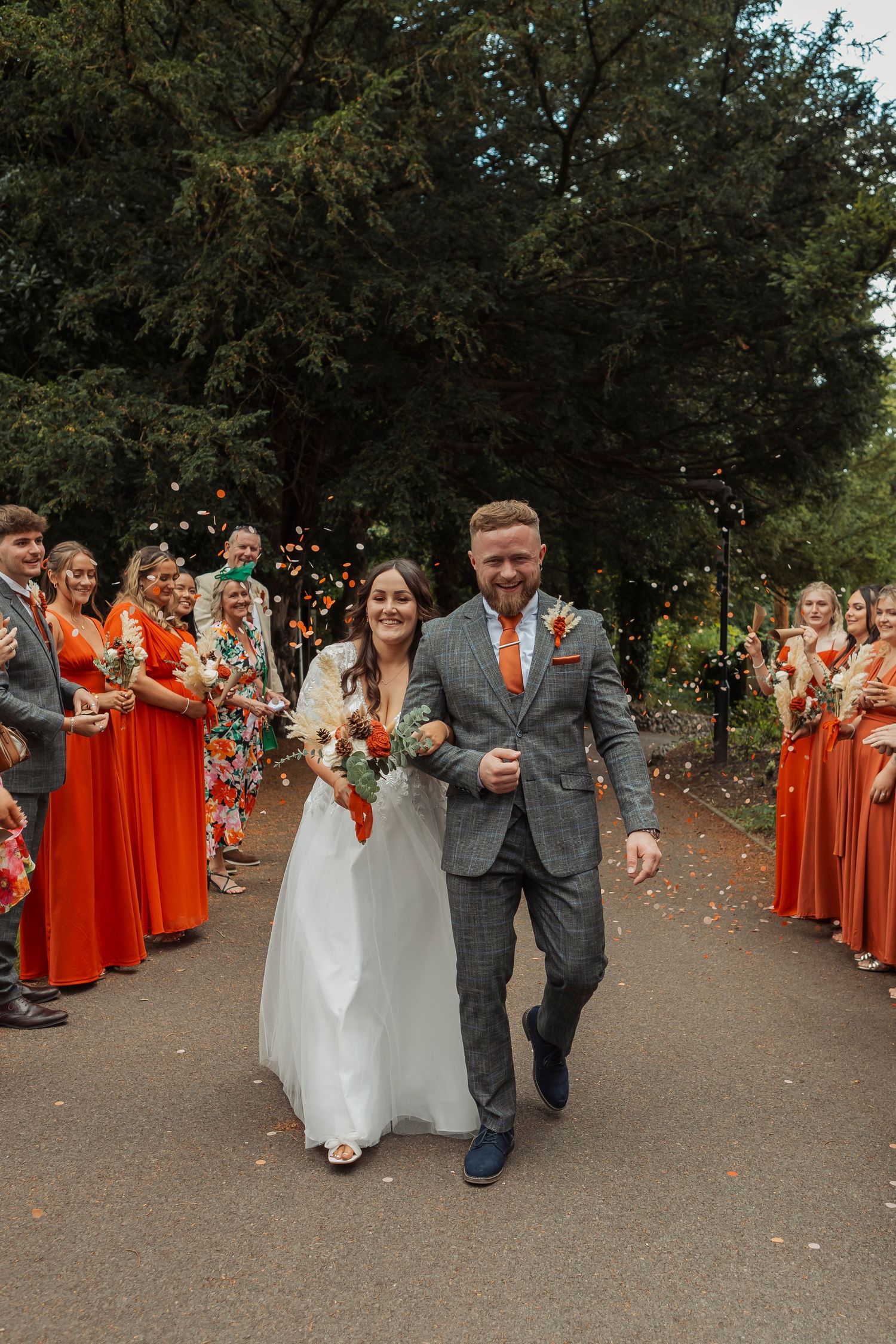 Wedding exit with guests in red dresses throwing confetti as couple walks down path.