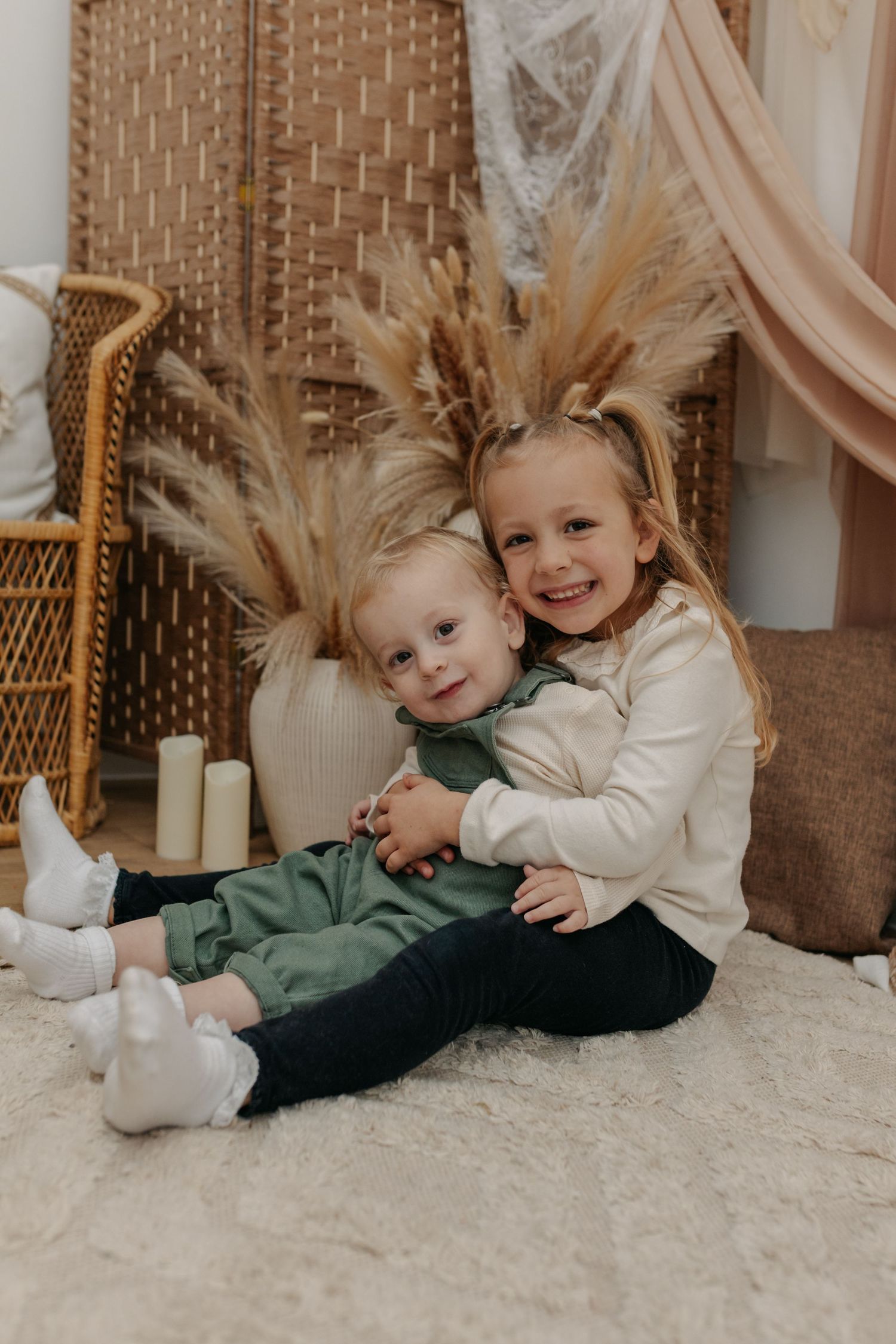 Children playing and cuddling on white carpet during photo session.