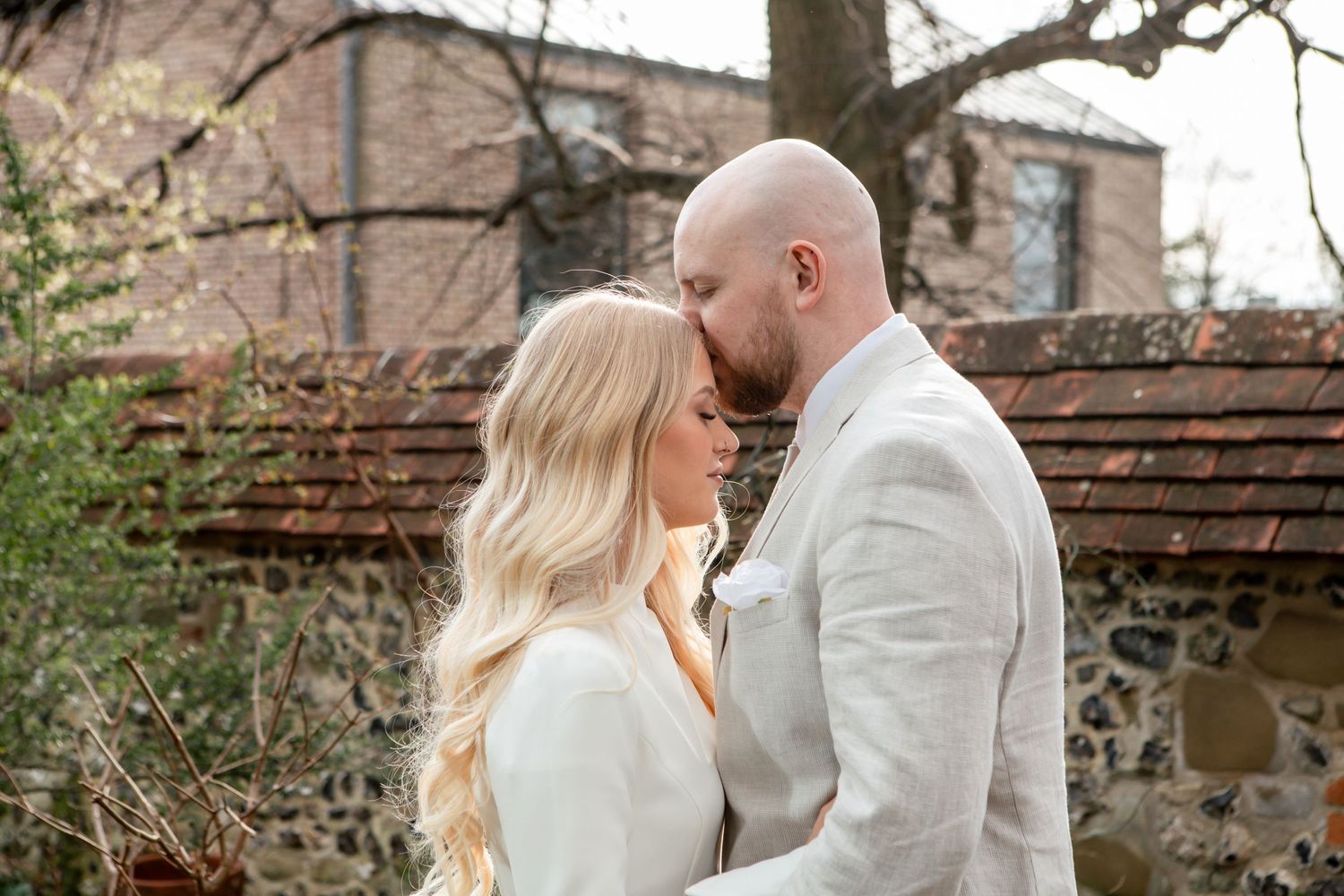 Couple sharing an intimate moment in white attire against a rustic garden background.