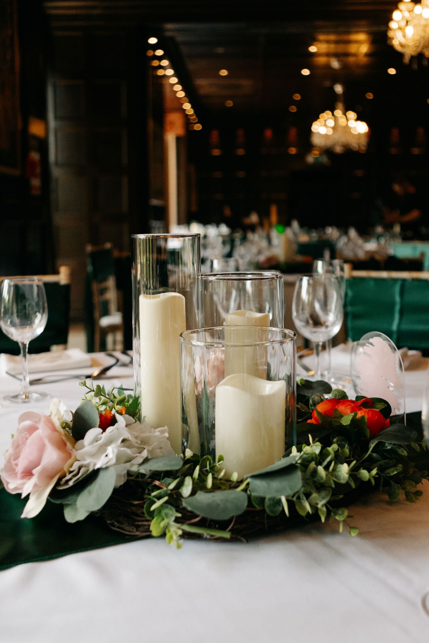 Wedding reception table decorated with white candles, greenery, and pink floral arrangements.