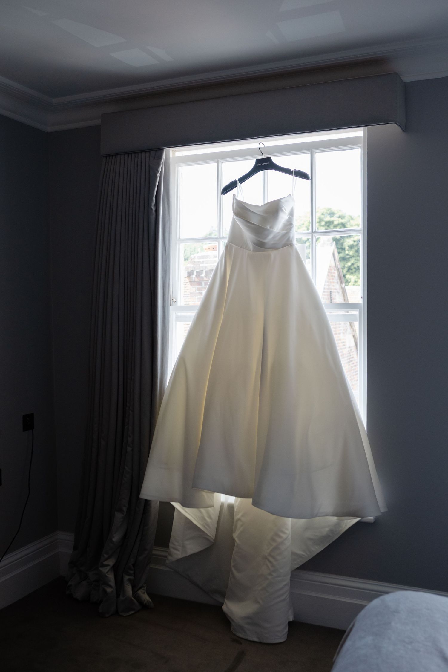 White wedding dress hanging in window with natural light streaming in.