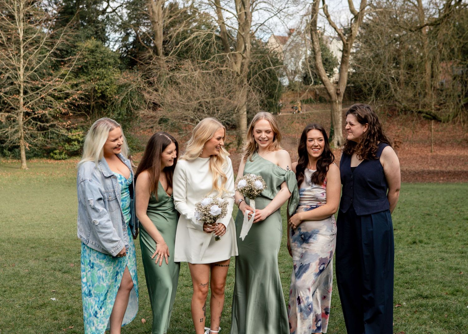 Wedding party poses together outdoors wearing sage green and floral dresses.