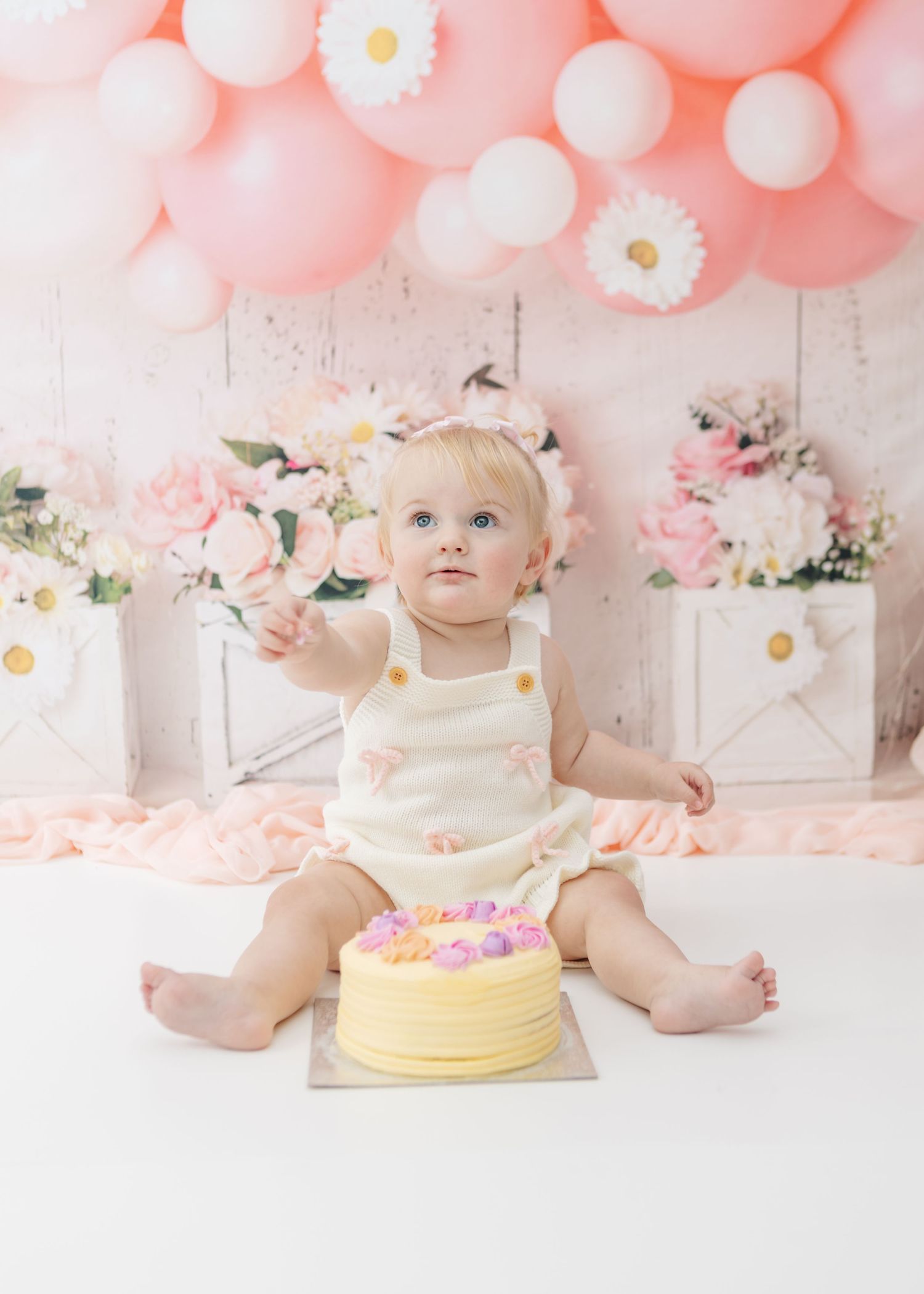 First birthday cake smash session with yellow cake and pink balloon decorations.