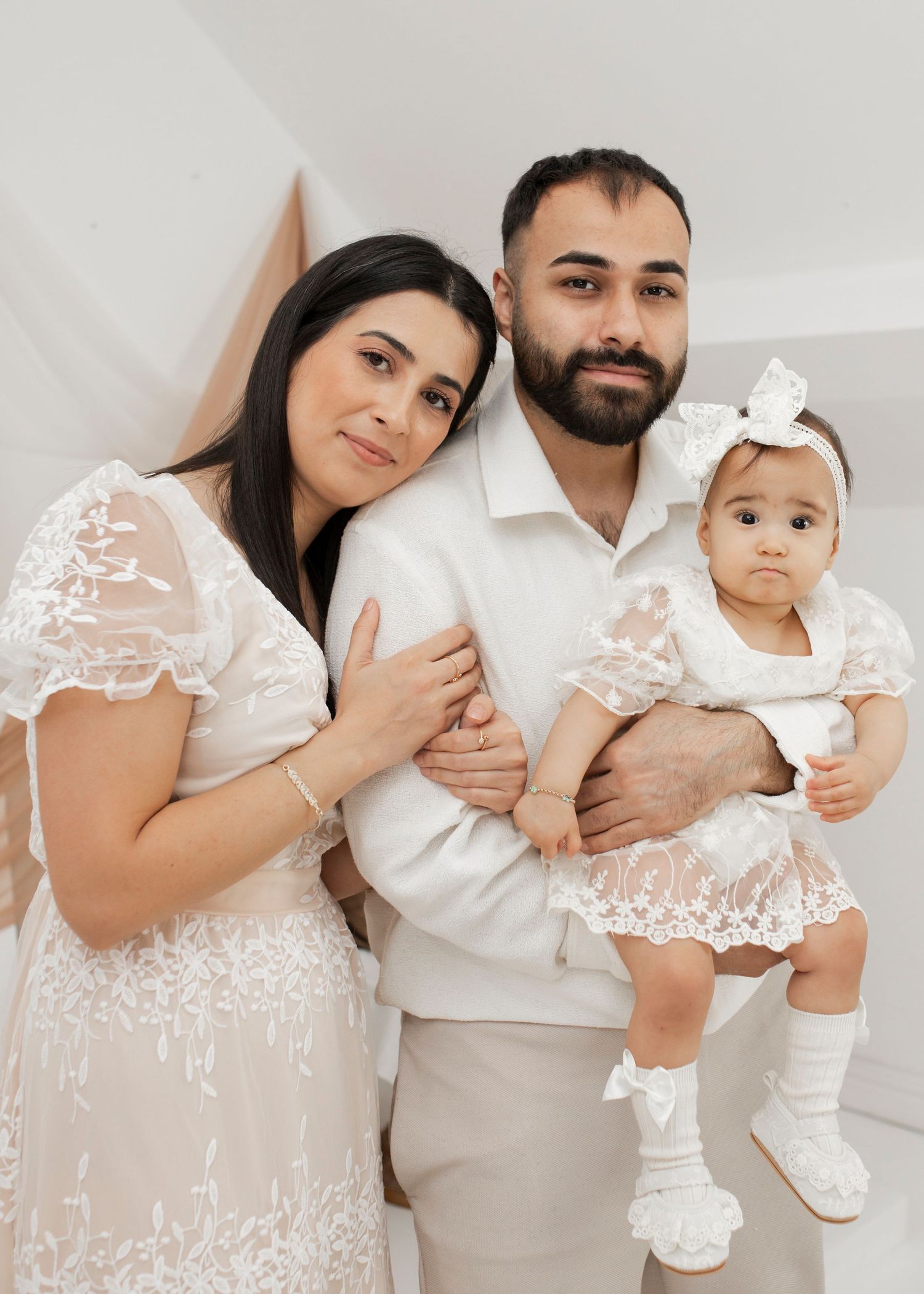 Family portrait in coordinated white and cream outfits against light background.
