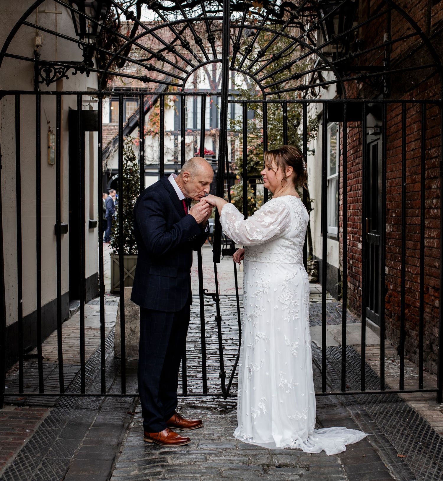 Newlyweds posing under decorative iron archway against brick walls.