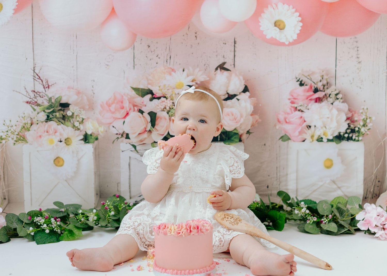 Pink and white themed cake smash photo setup with balloons and florals.