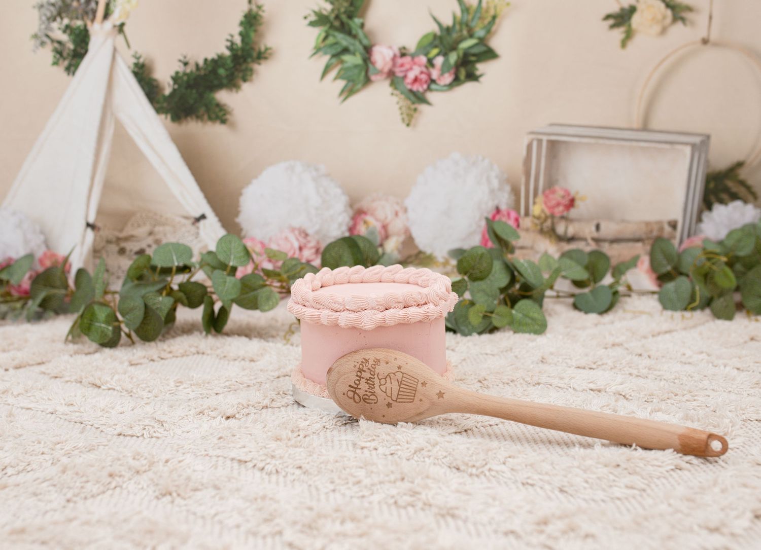 Rustic backdrop with greenery garlands and floral decorations for a cake smash photoshoot.