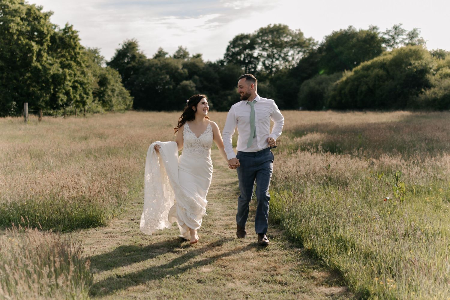 Couple walking hand in hand through a golden field at sunset.