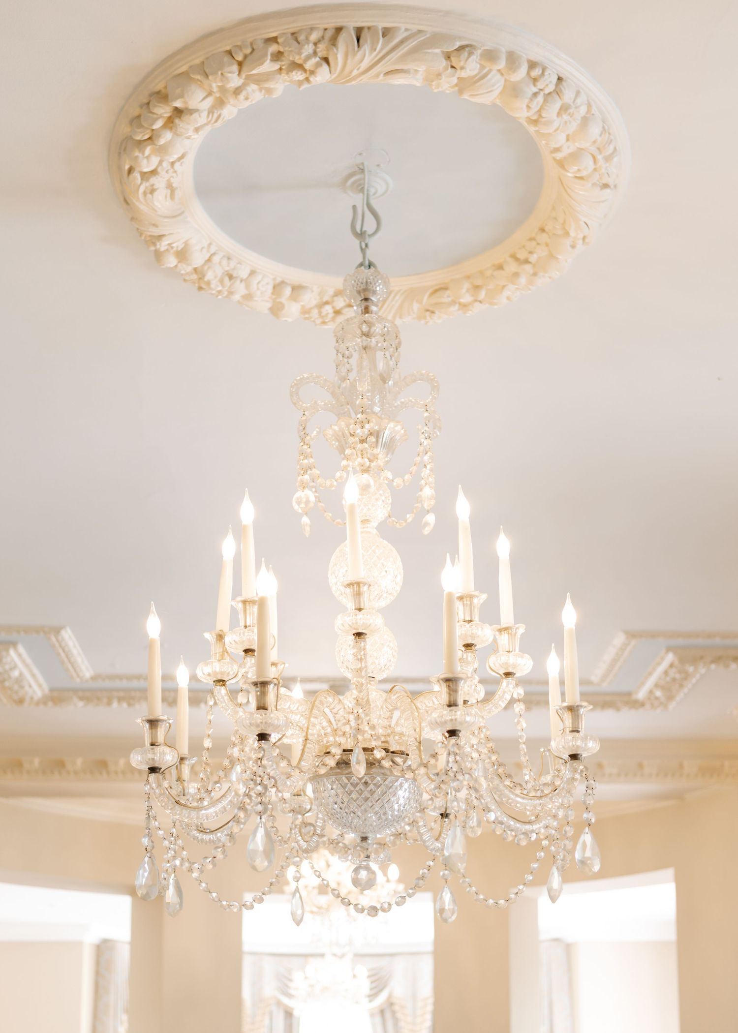 Crystal chandelier with ornate ceiling medallion in a formal white room.