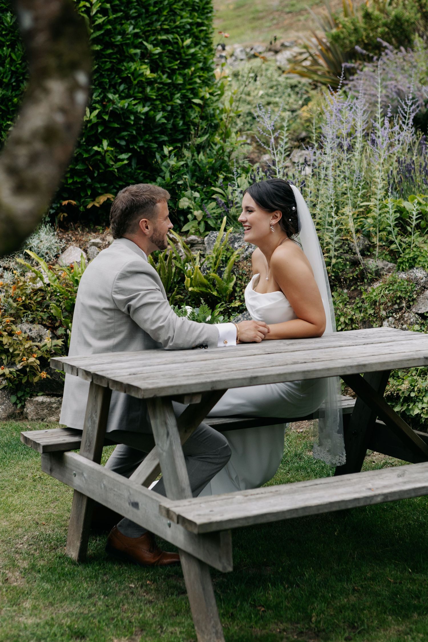 Couple shares intimate moment while sitting at wooden picnic bench in garden setting.
