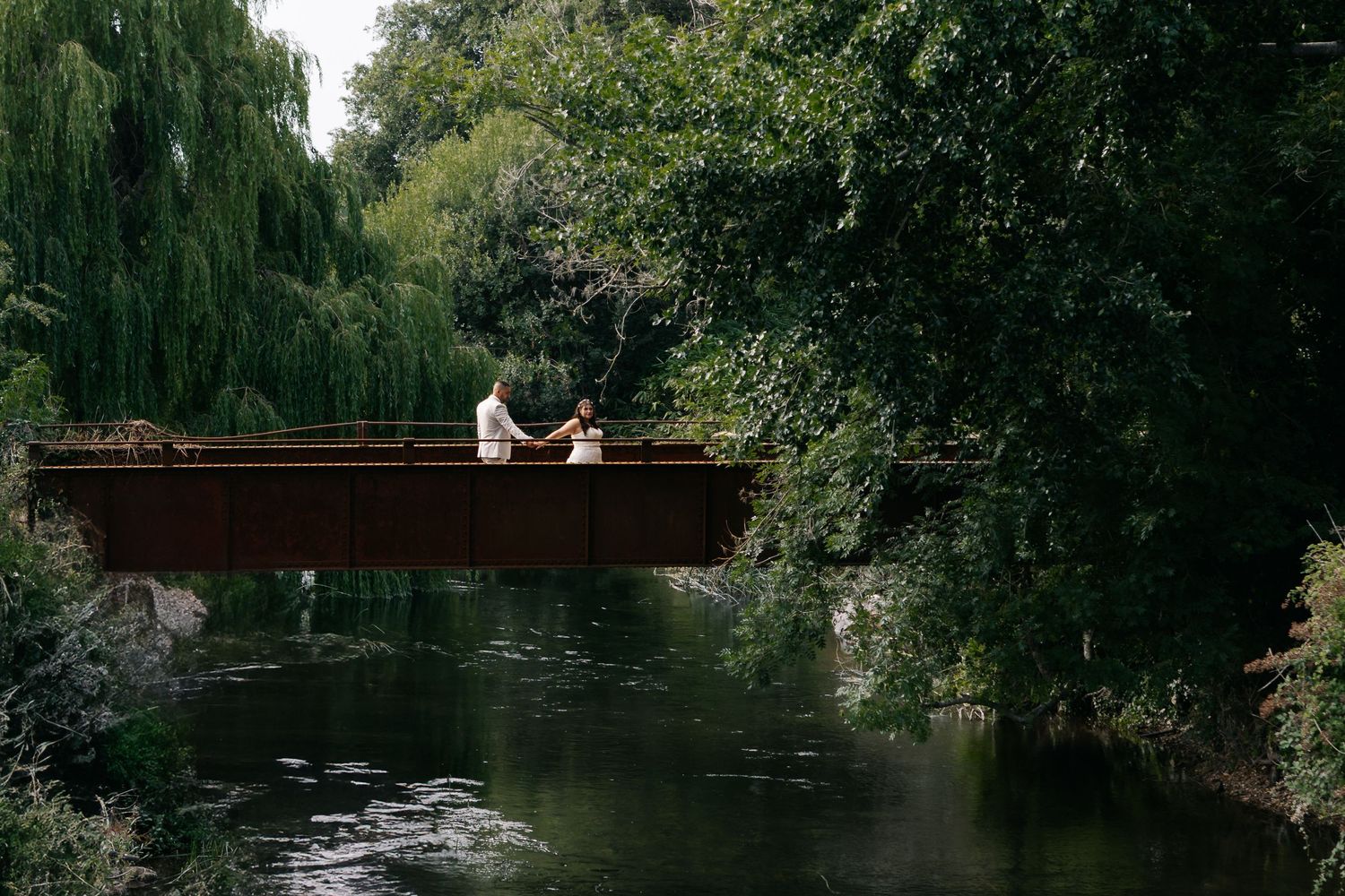 Scenic pond with weeping willow trees and wooden bridge in background.