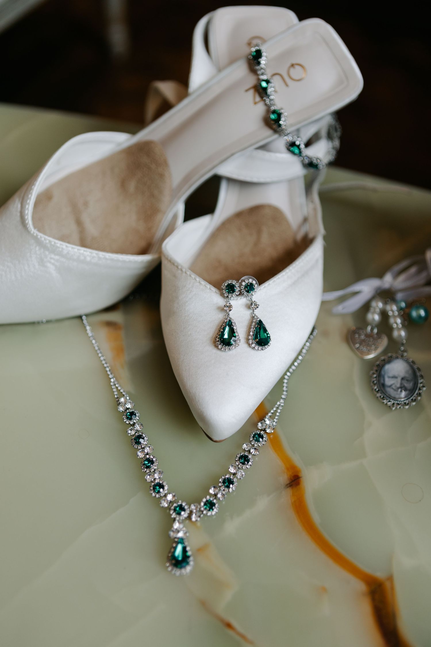 White bridal shoes with emerald jewelry and accessories displayed.