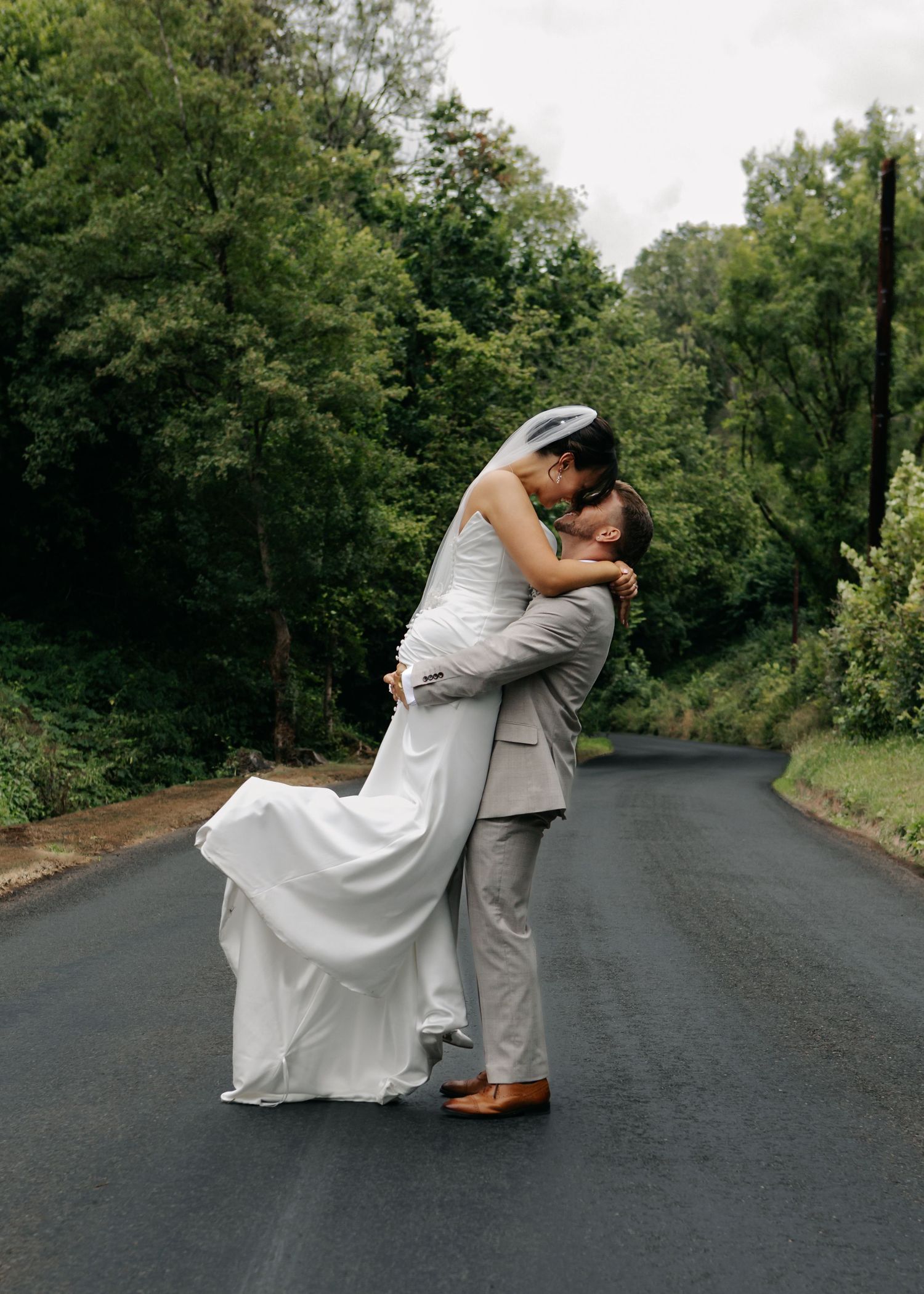 Wedding couple embraces on an empty road surrounded by trees.
