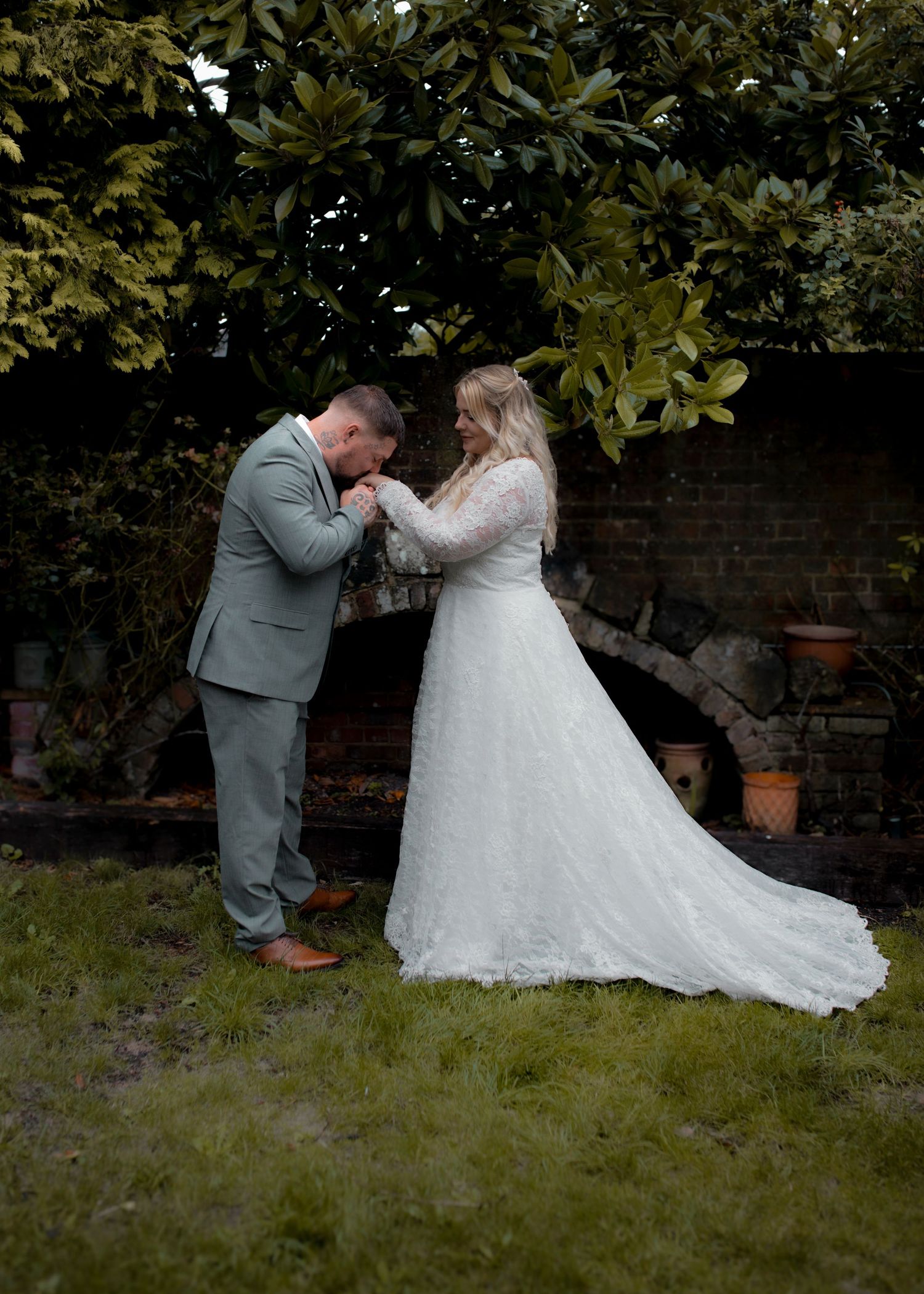 Wedding couple sharing an intimate moment on grass under trees in a garden setting.