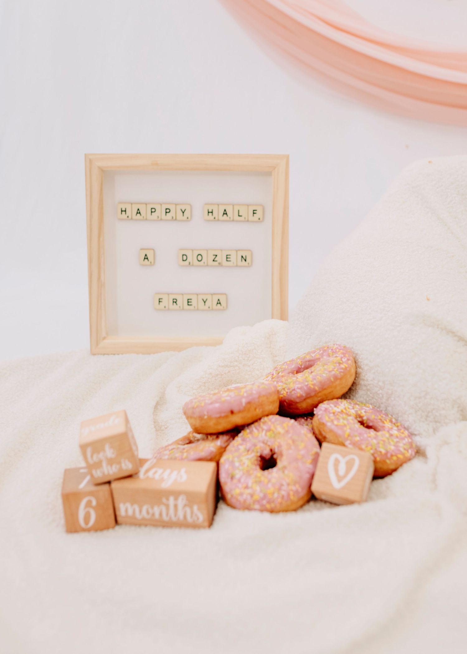 Letter board and wooden blocks arranged with pink donuts for baby milestone photography.