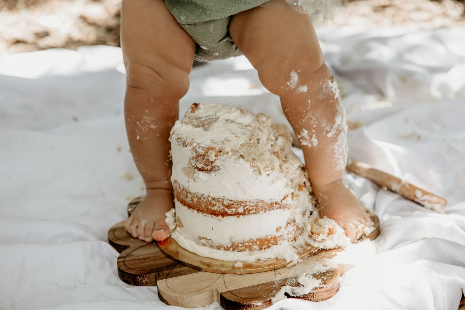 Messy cake smash scene with frosting scattered across white fabric.