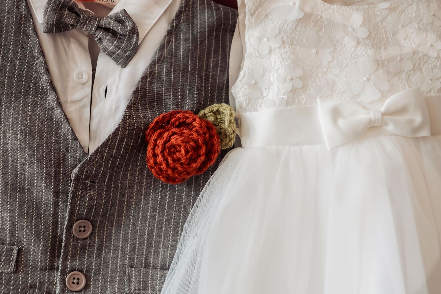 Close-up of wedding attire details showing a red boutonniere against a striped vest and white dress.