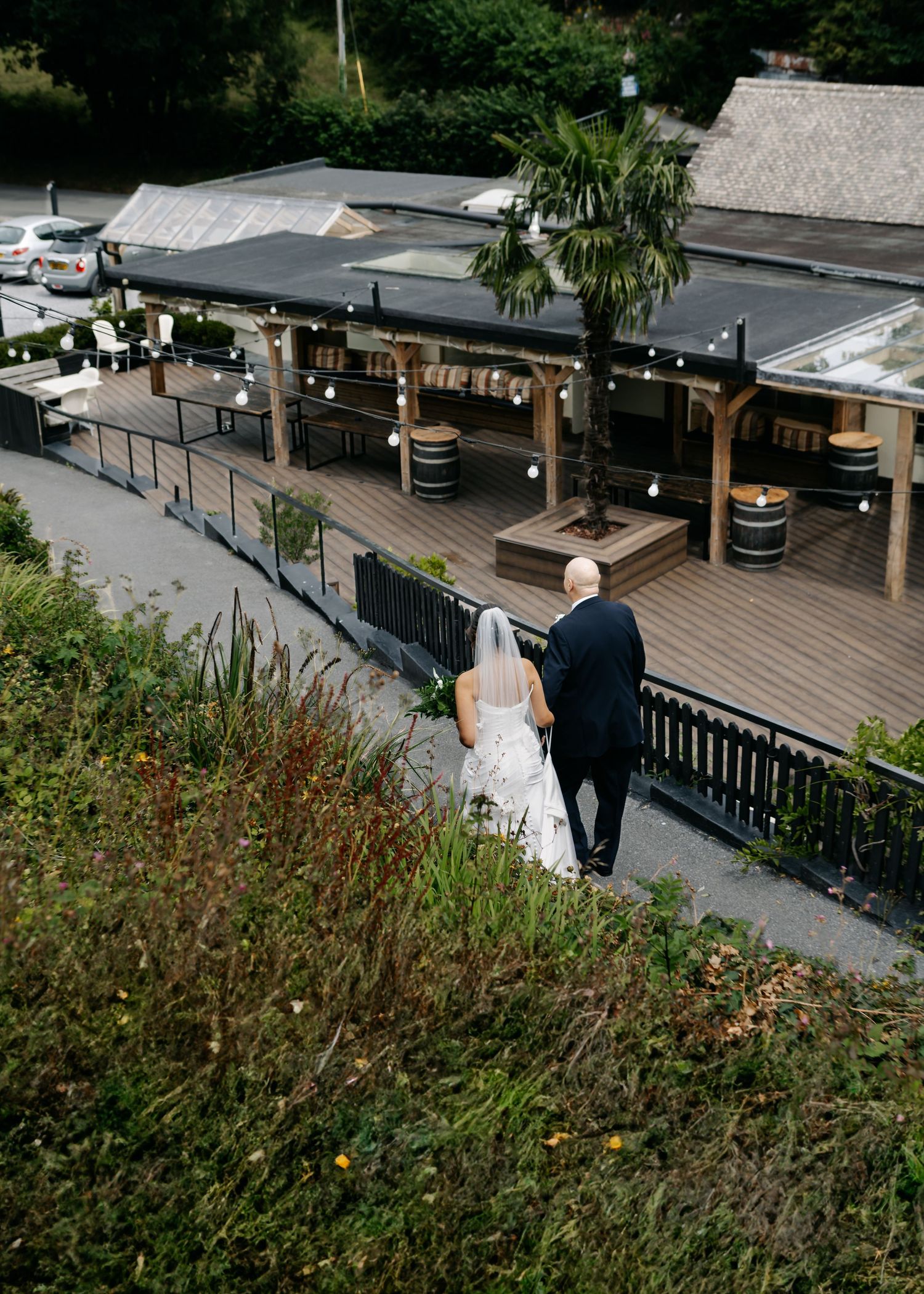 Couple overlooking an outdoor venue with wooden deck and barrel decorations from a hilltop.