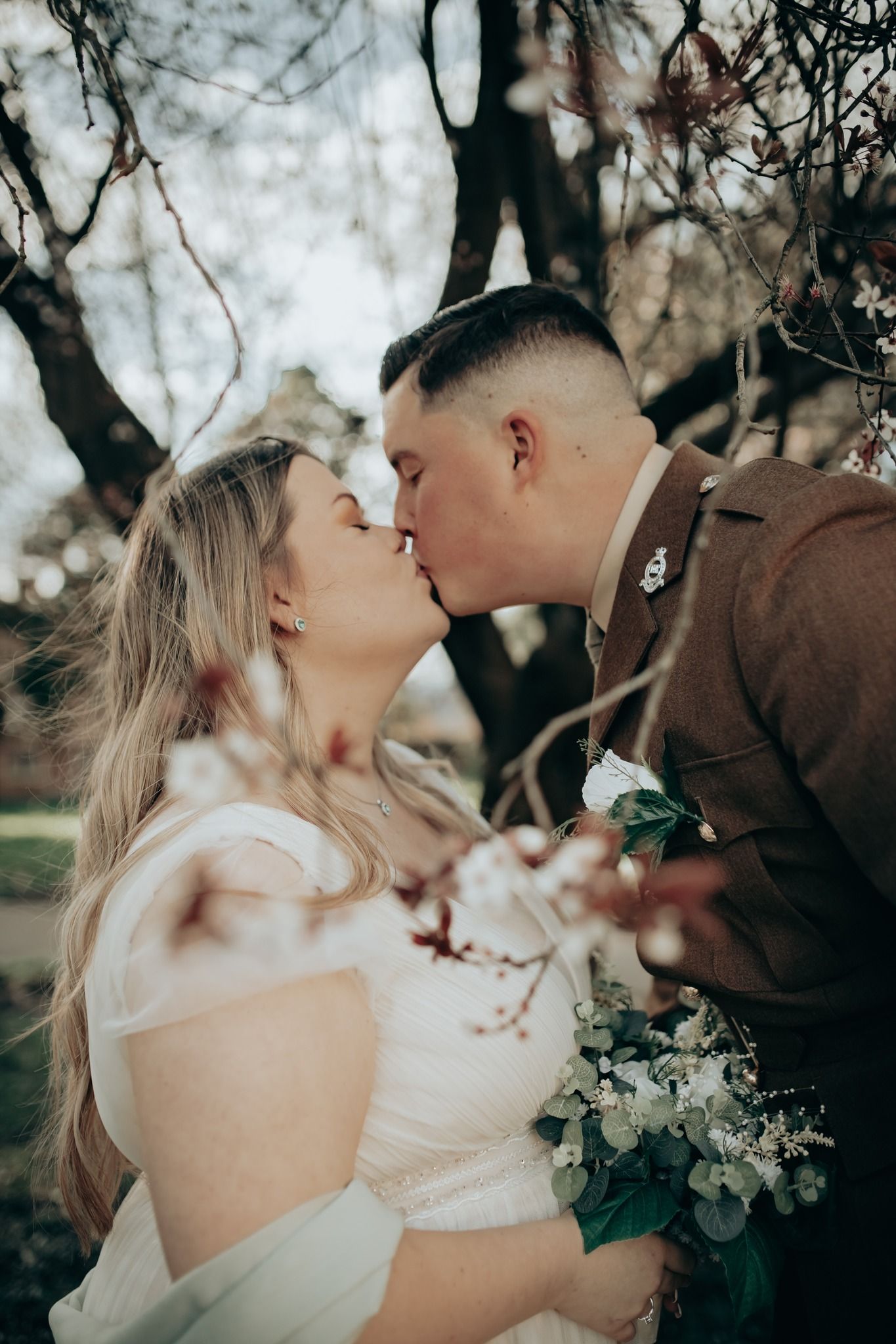 Romantic wedding portrait under blooming spring trees with soft natural lighting.