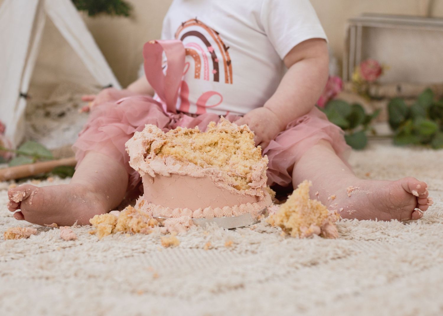 Messy cake smash scene with crumbs scattered on light carpet.