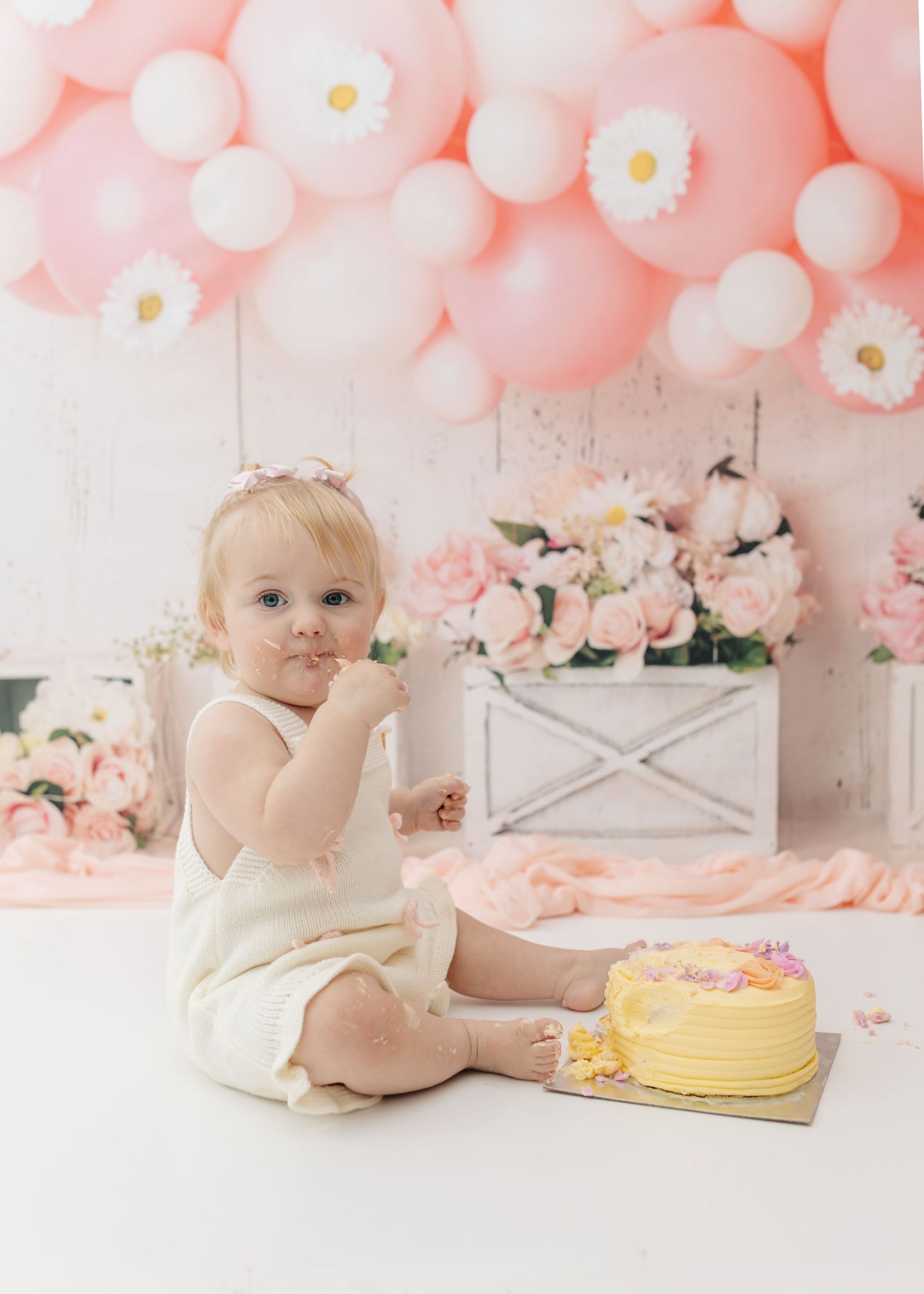 First birthday celebration setup with yellow cake and pink balloon arch for cake smash photos.