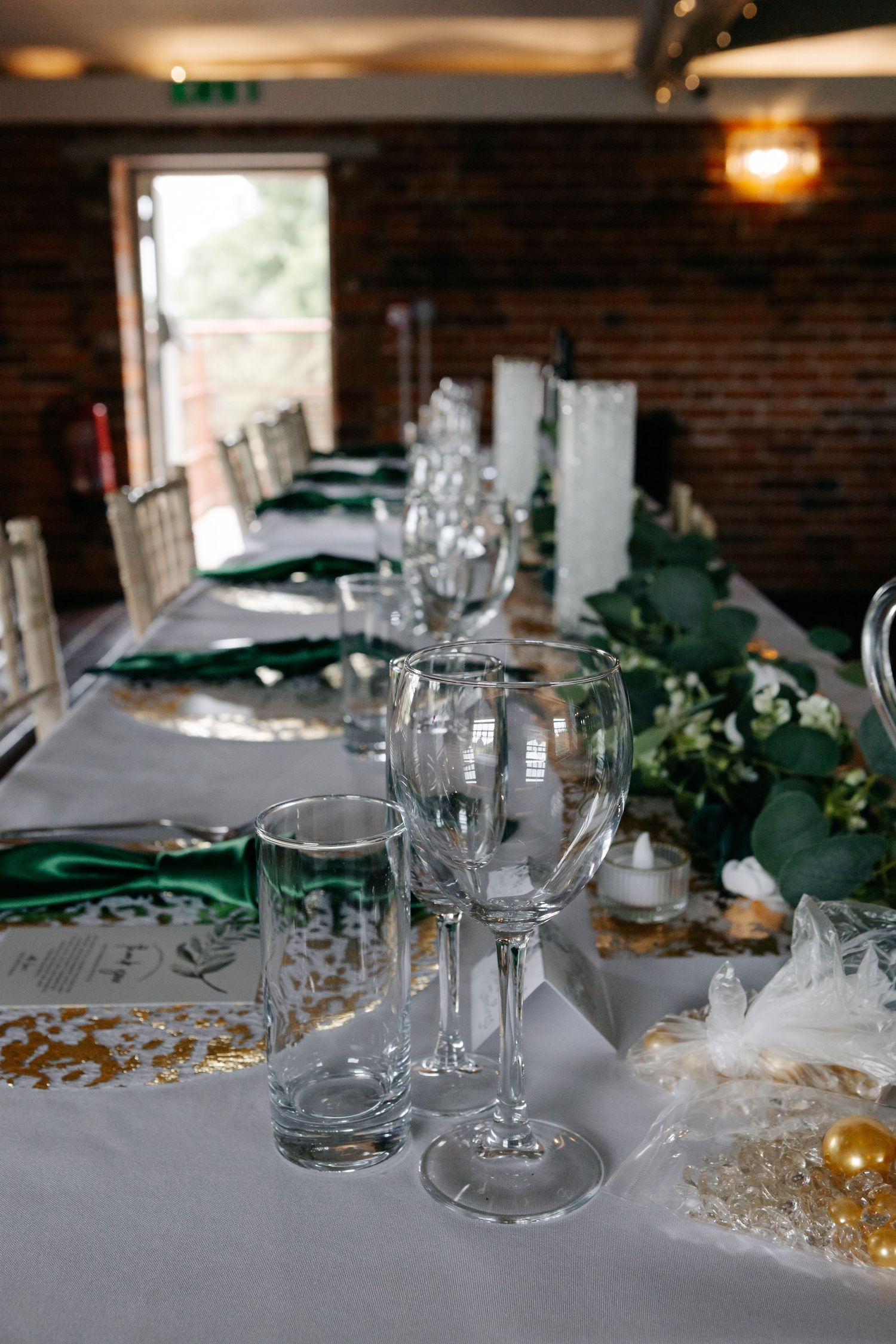 Elegant wedding reception table setting with glassware and green accents.