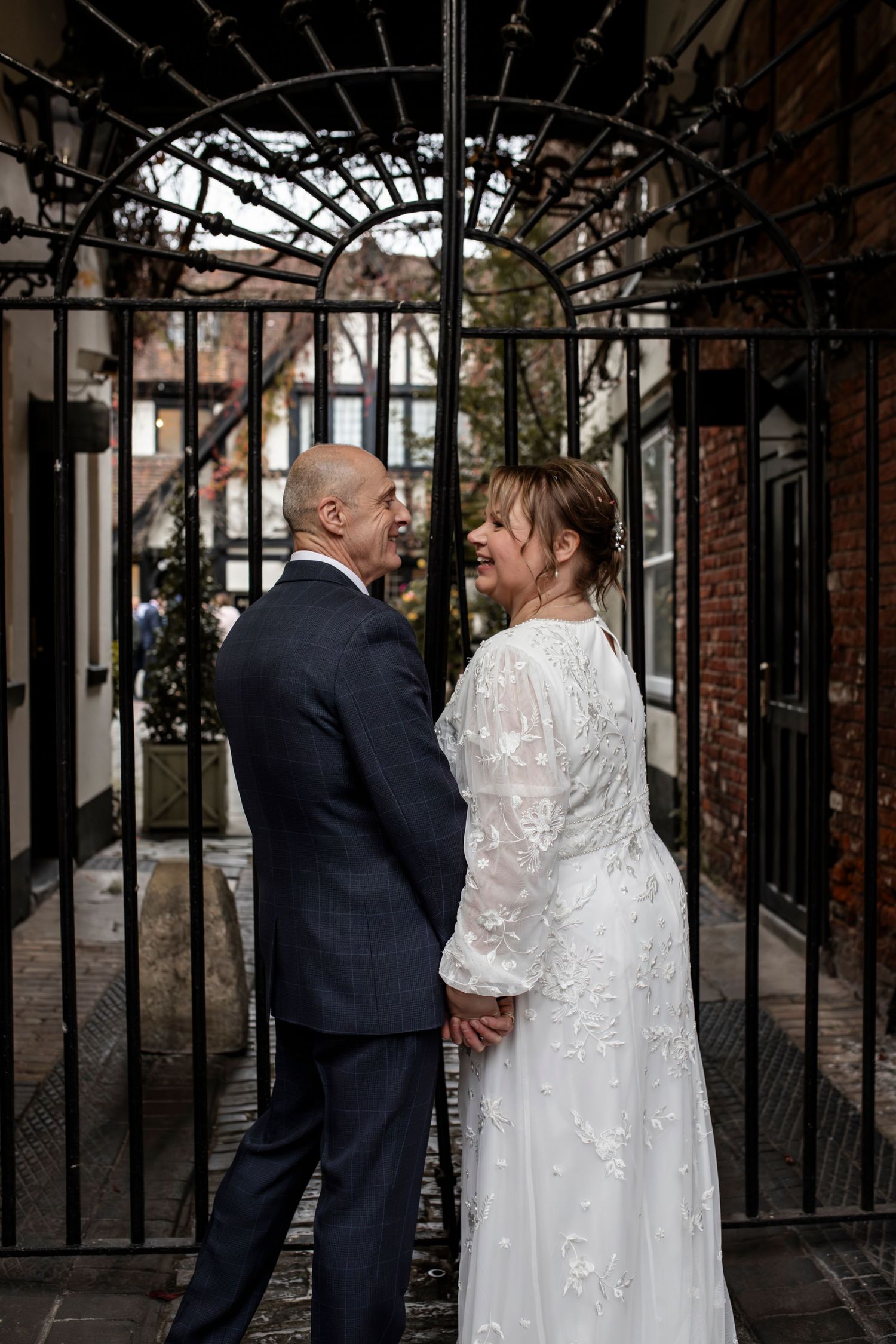 Romantic wedding portraits under vintage iron archway with brick backdrop.