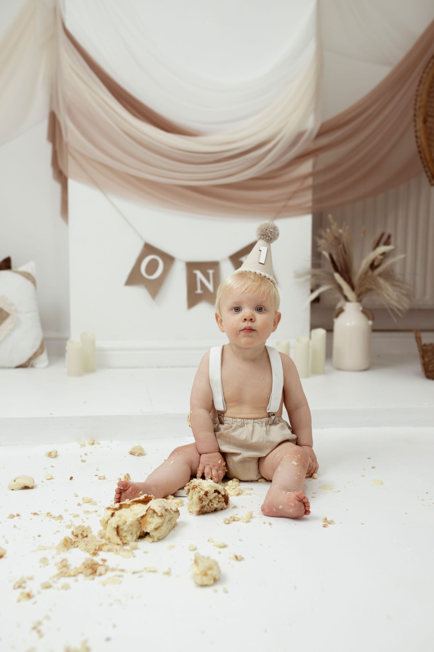 Cake smash aftermath with crumbs scattered on white floor beneath rustic banner.