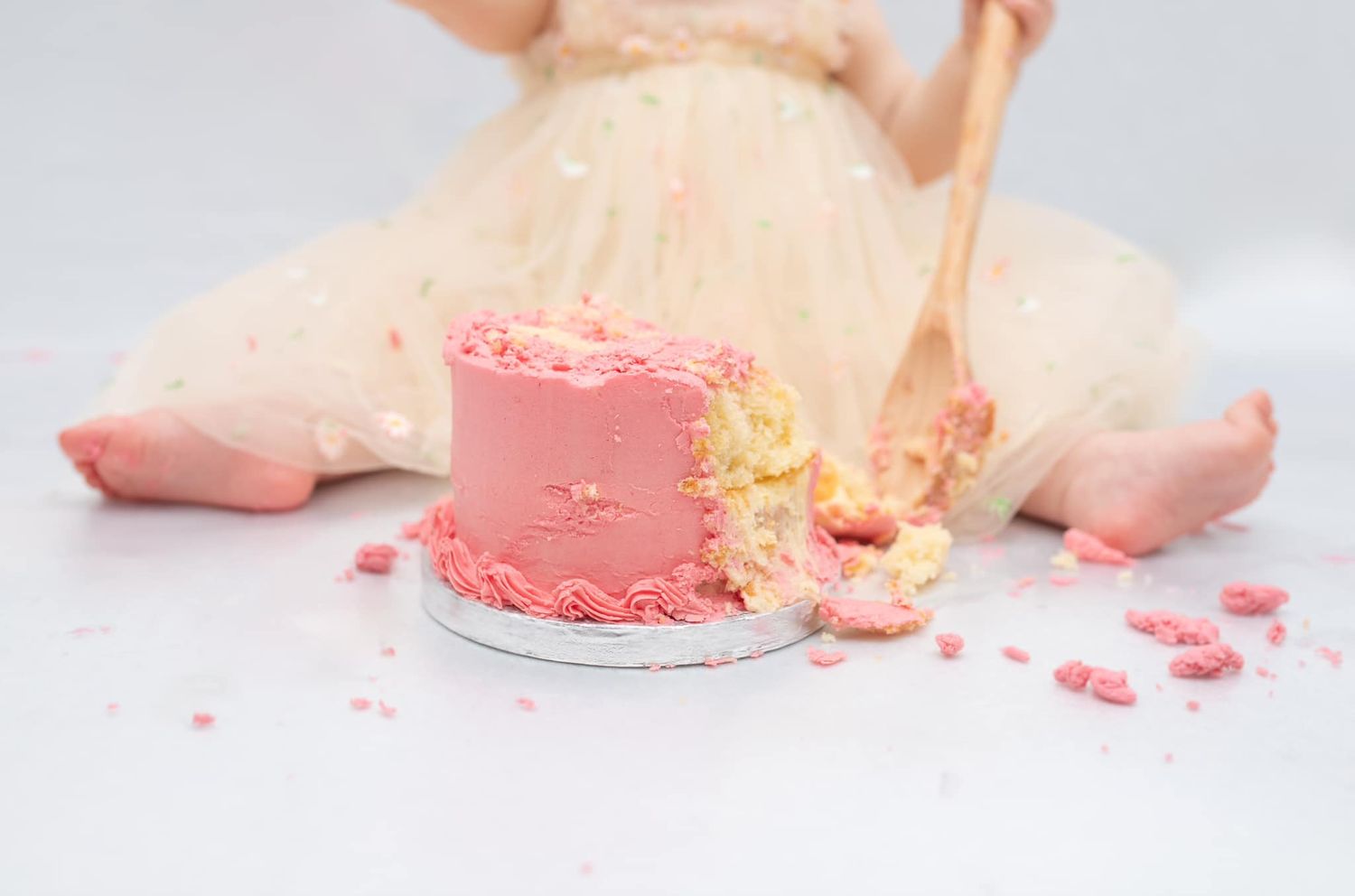 Pink frosted cake being smashed and crumbled during a cake smash photo session.