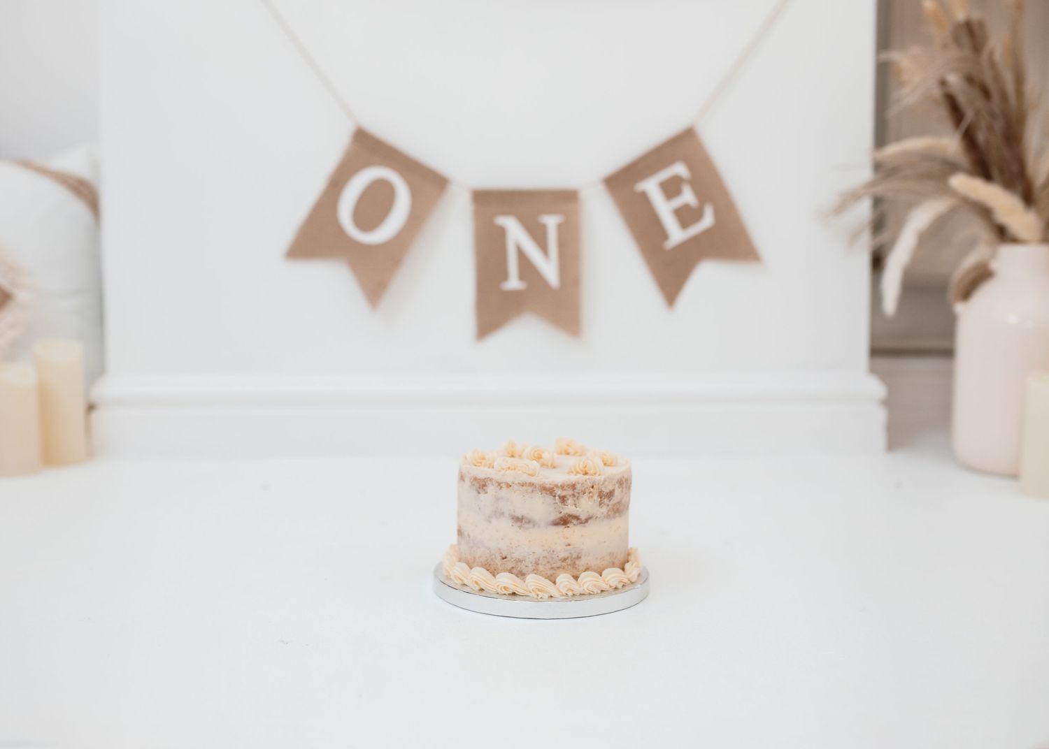 Simple white cake with 'ONE' banner decoration for first birthday celebration.