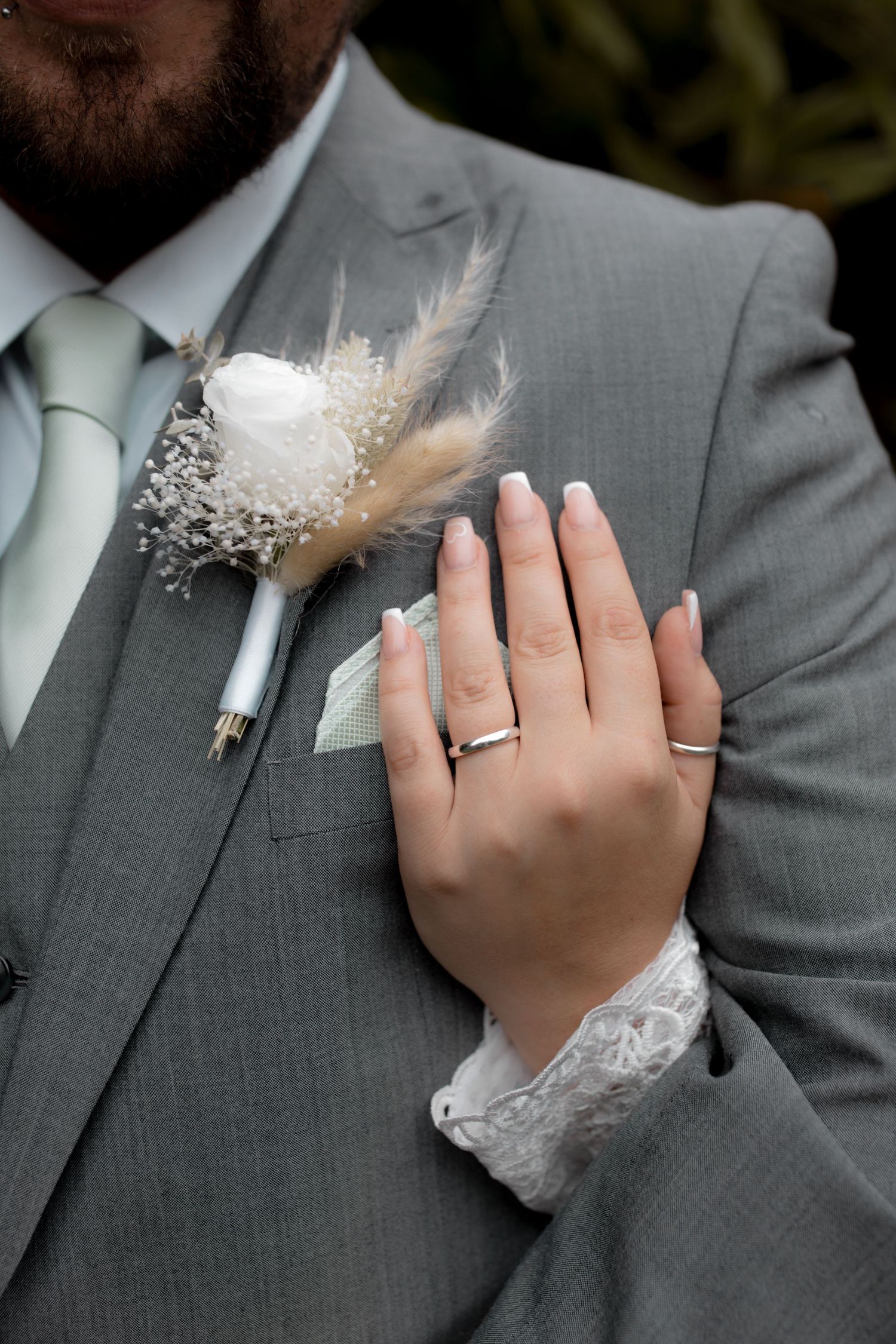 Close-up of a gray suit lapel with white floral boutonniere and lace details.