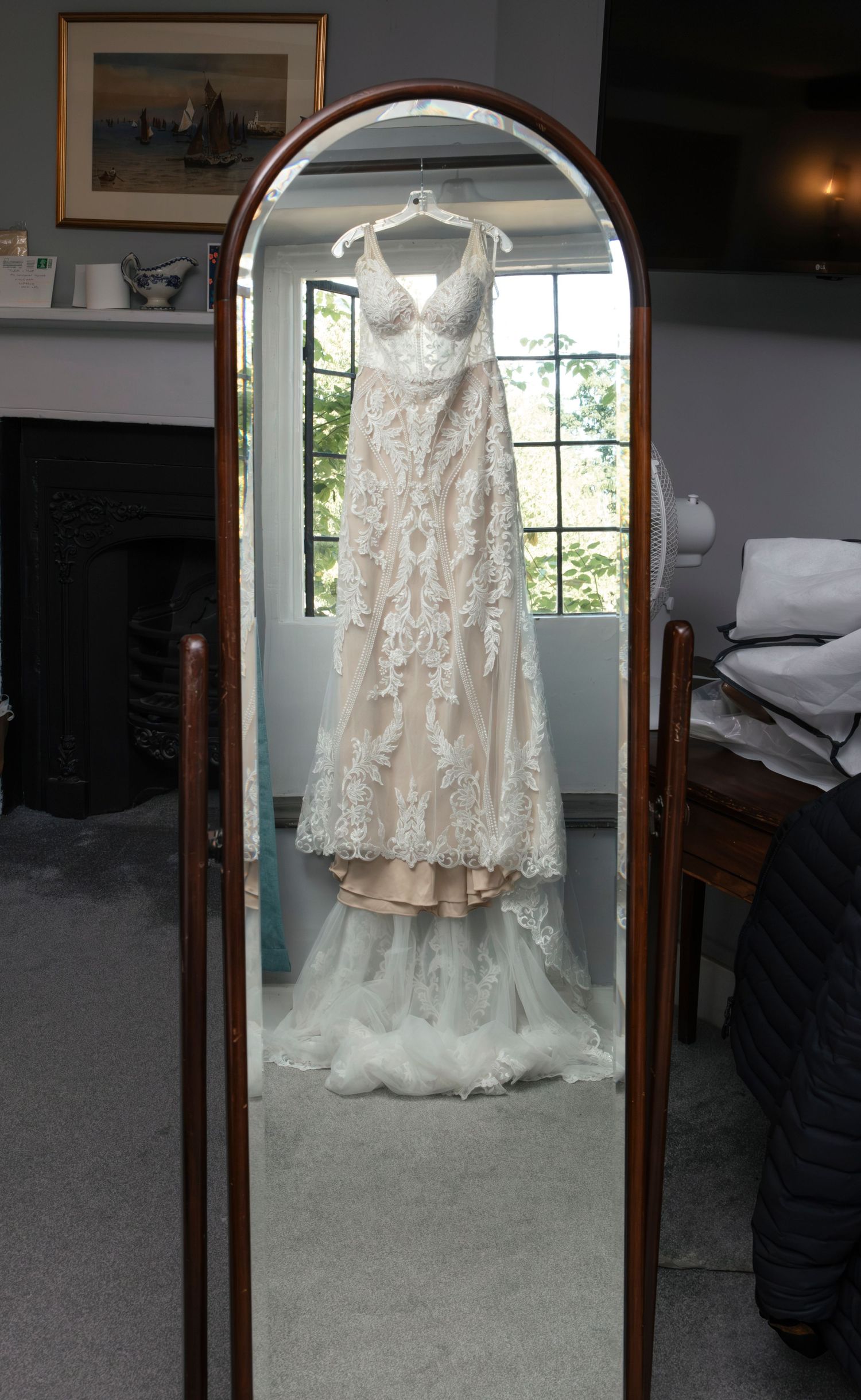 Beautiful lace wedding dress displayed in a full-length mirror with wooden frame.