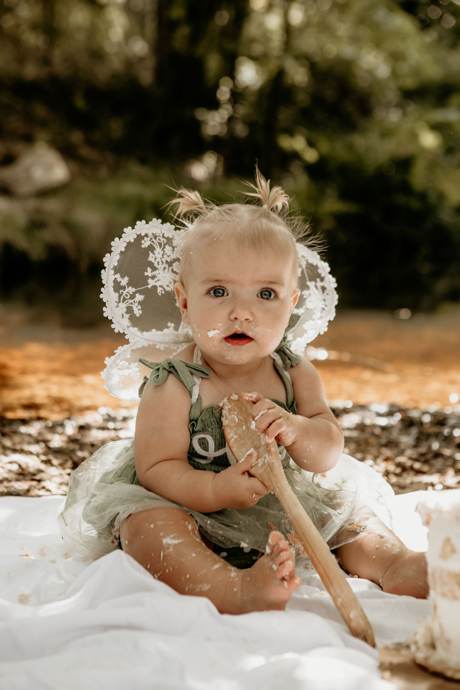 Cake smash photography session with white flowers and sage green outfit.