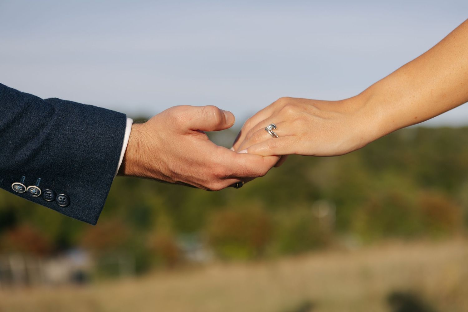 Close-up of hands exchanging rings during an outdoor wedding ceremony.