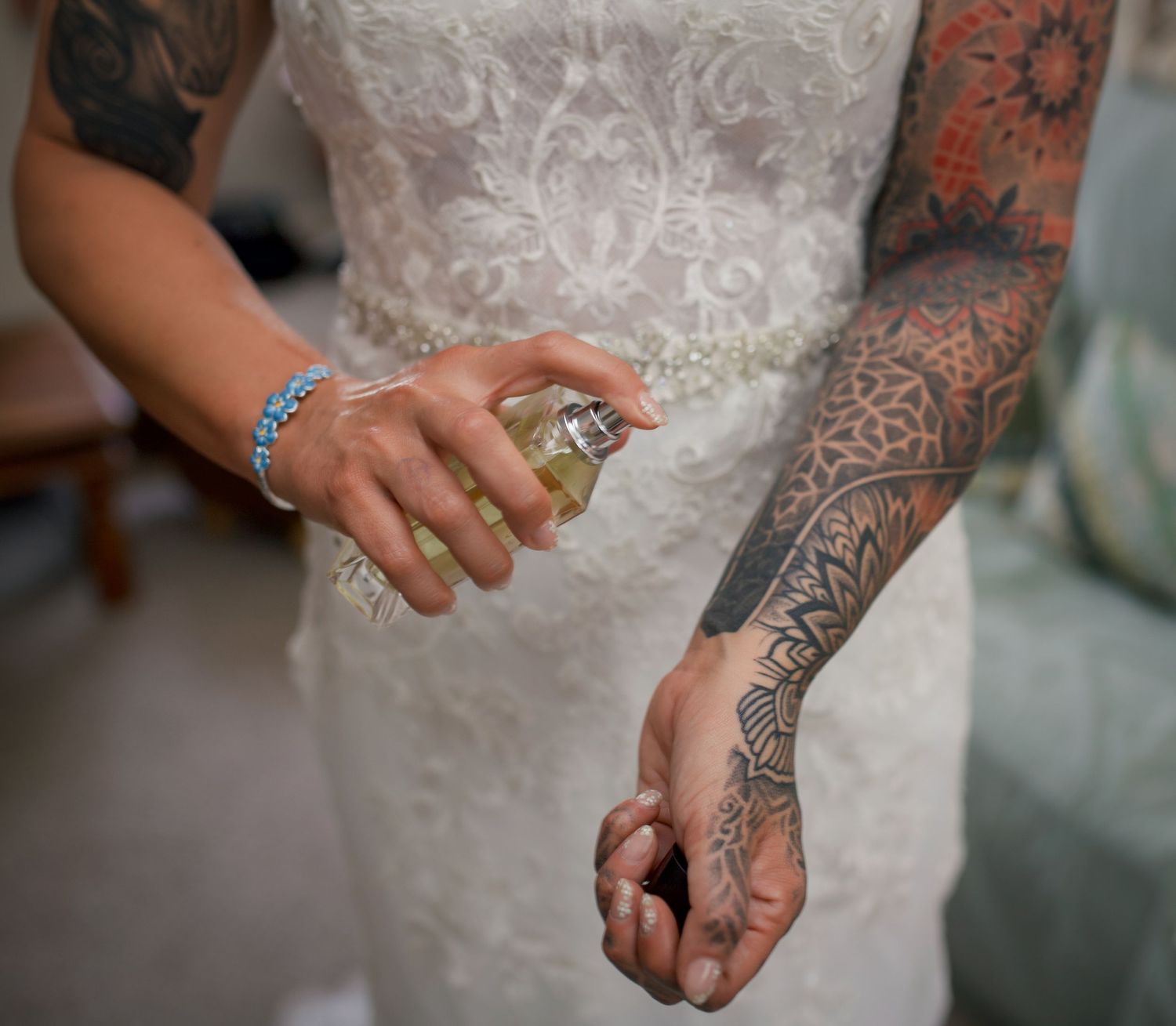 Detailed view of tattooed arms against white lace wedding dress.